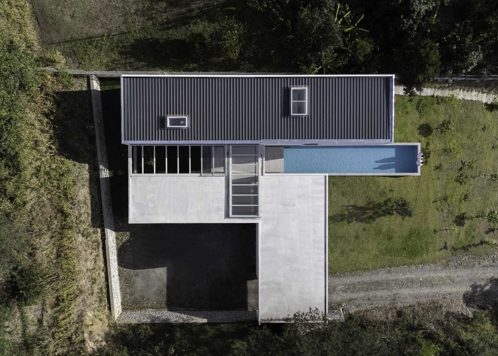 A modern house with a concrete floor plan, featuring a rooftop deck, large windows, and a swimming pool.
