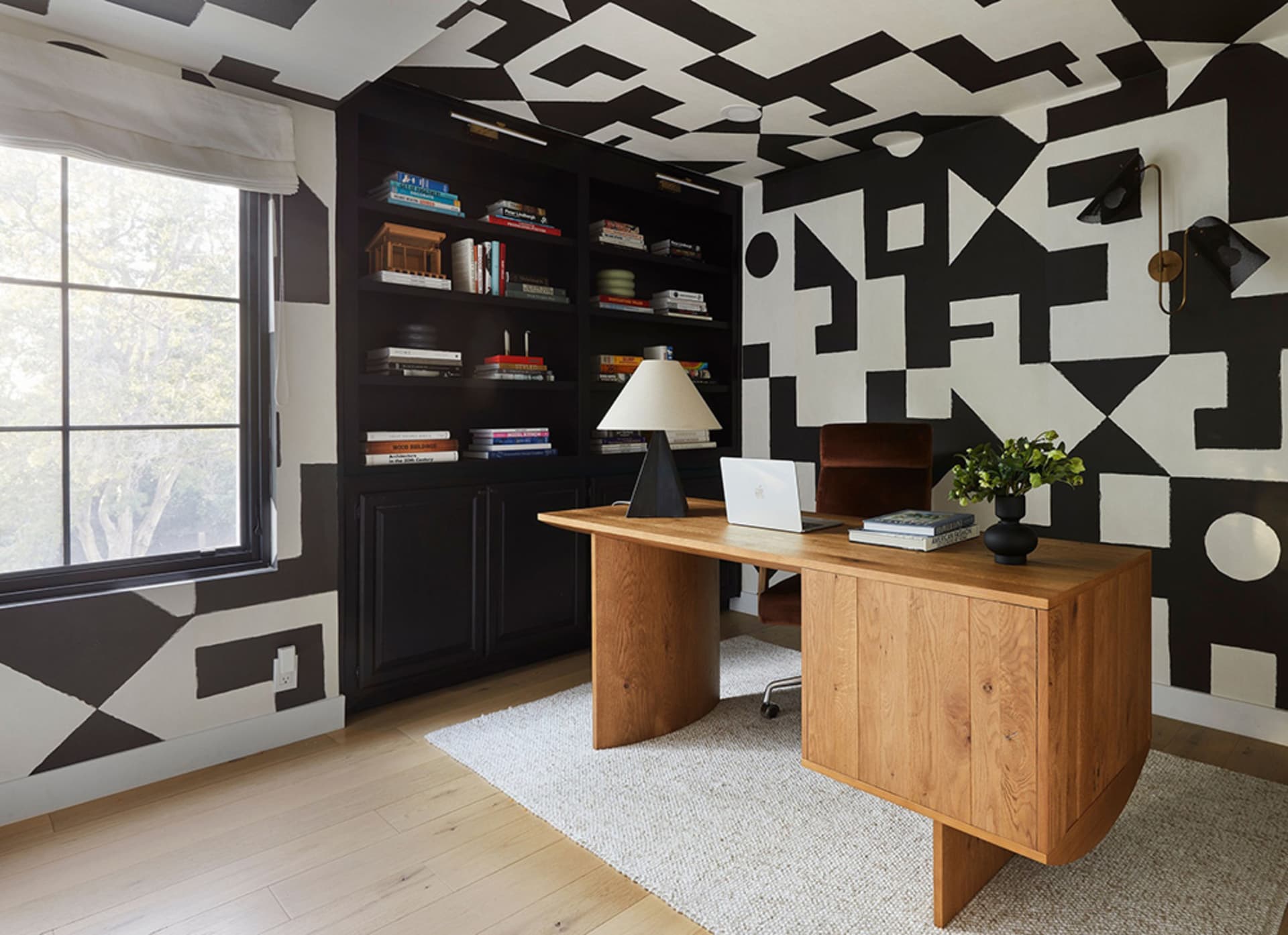 A modern office space featuring a wooden desk with a laptop, lamp, and books.