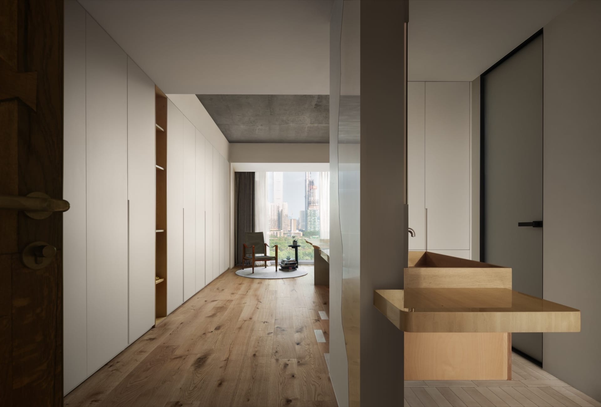 Interior view of a modern apartment with white walls, a concrete ceiling, wooden flooring, and a balcony with a cityscape vie