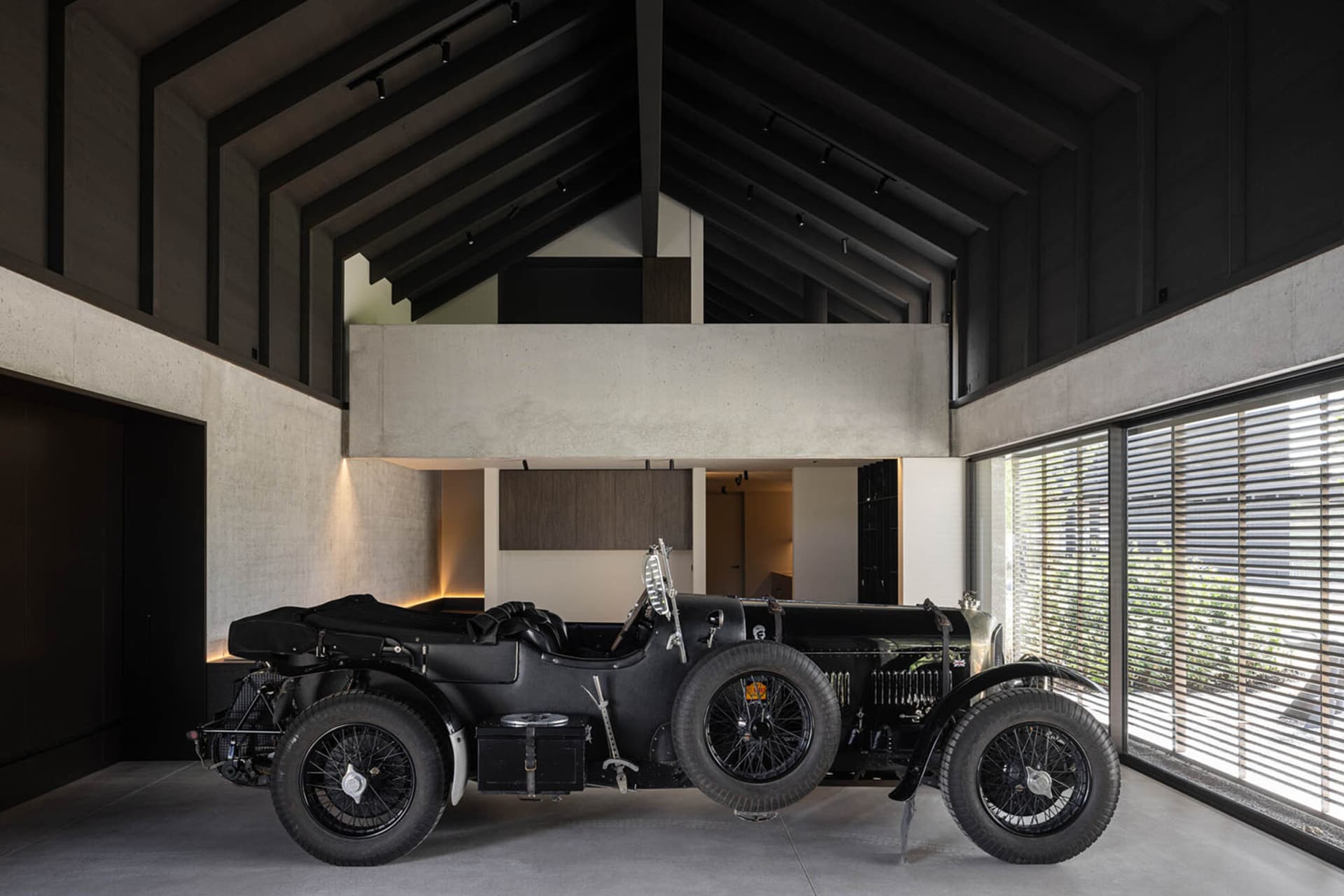 A vintage black car parked in a spacious garage with concrete walls and high ceilings.