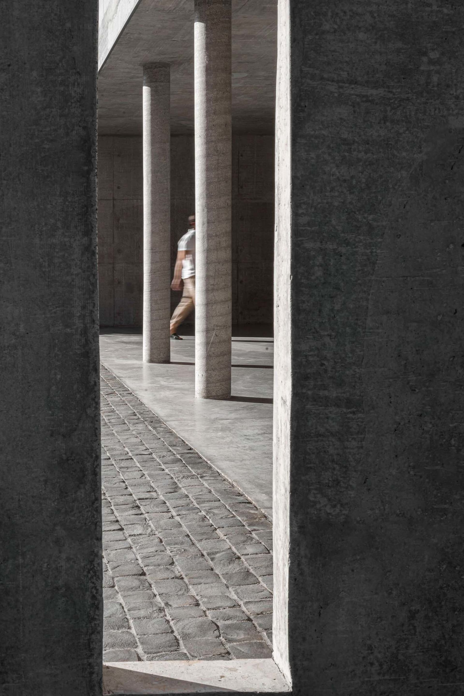 A minimalist concrete pathway with tall white columns on a grey concrete background.