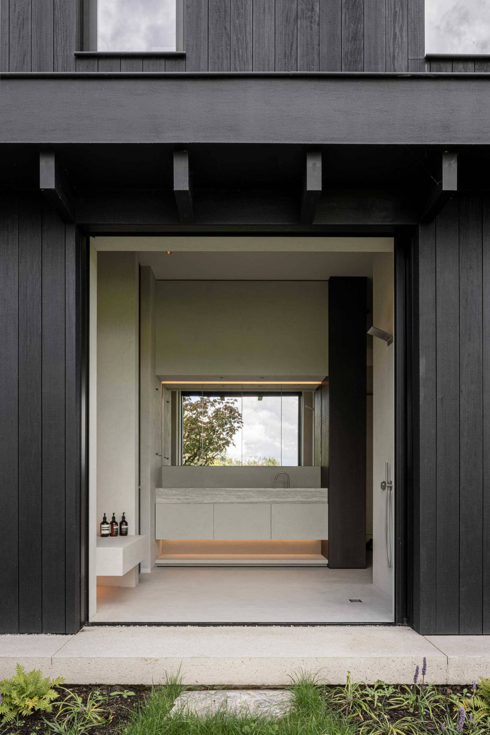 A modern, minimalist bathroom with concrete walls and floor, glass partition, and a sink with a large mirror.