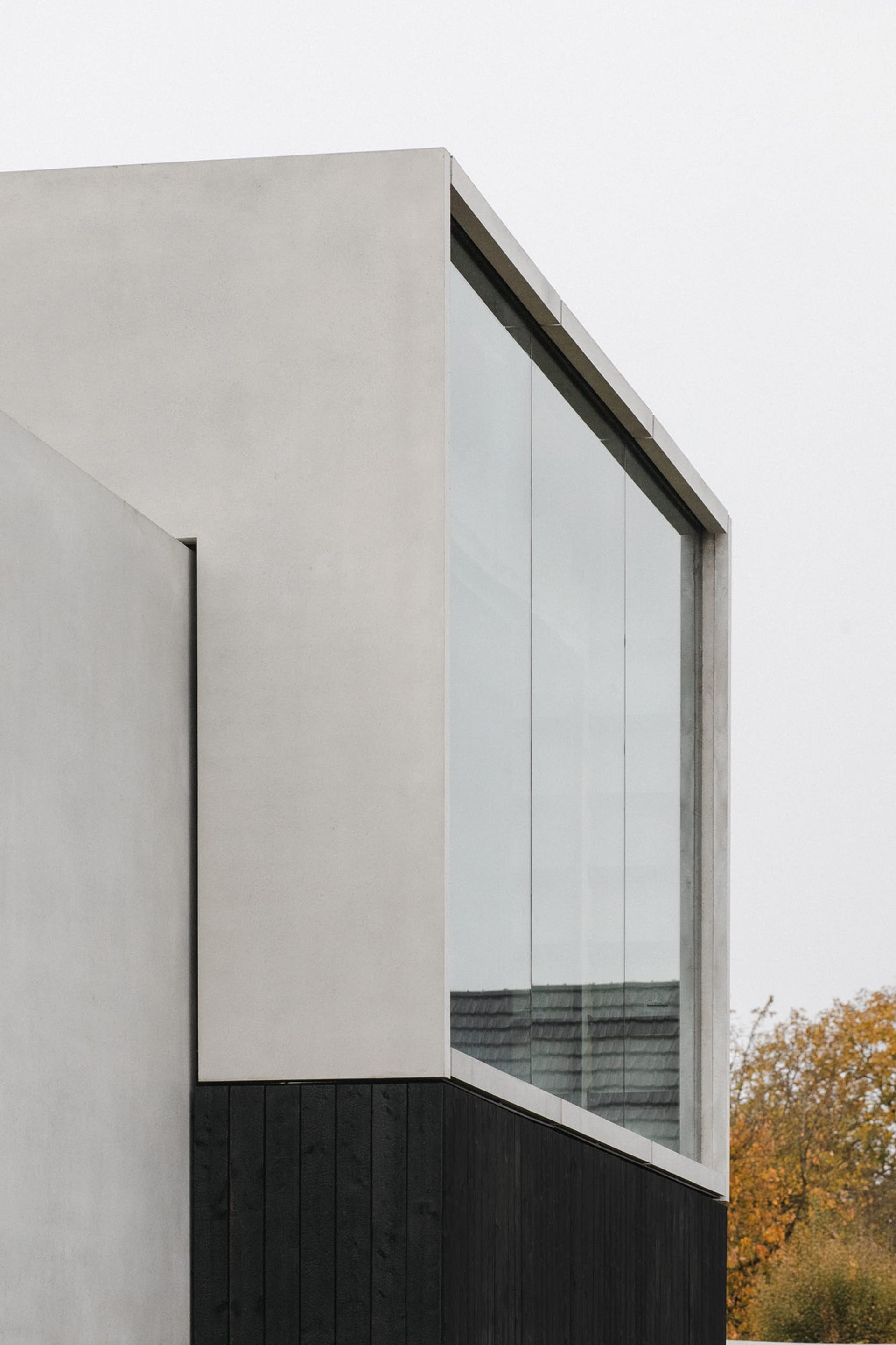 Modern architectural exterior featuring concrete and black wooden panels with a large glass window.