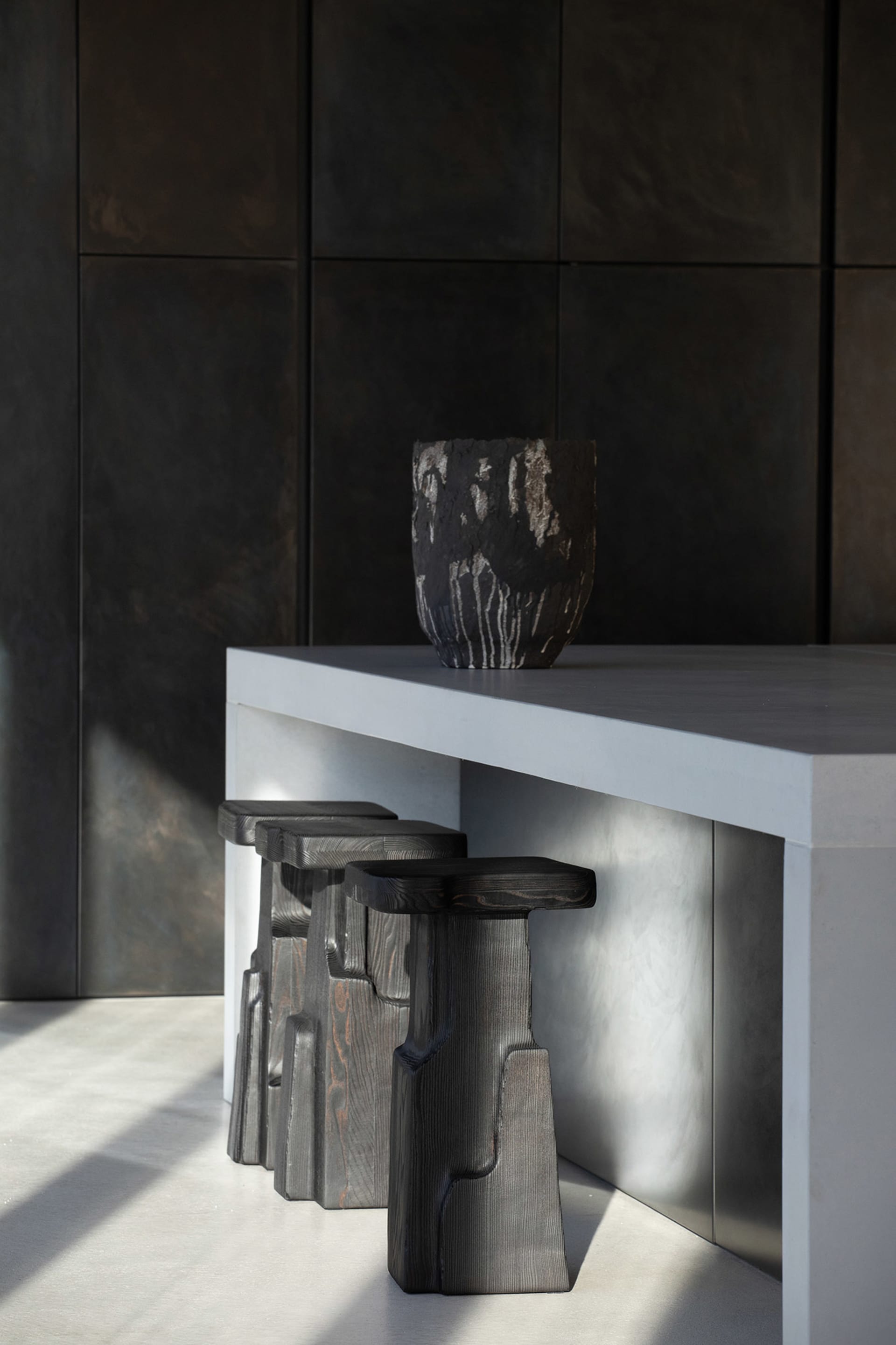 Modern kitchen interior with concrete countertops, stools, and wall panels.