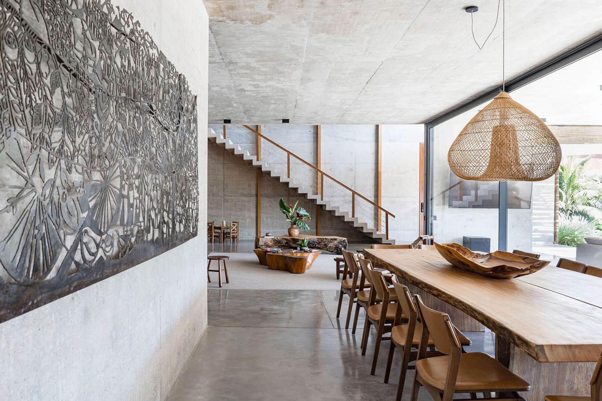 Modern dining room with industrial design, featuring concrete walls, a wooden dining table, and a decorative wall hanging.