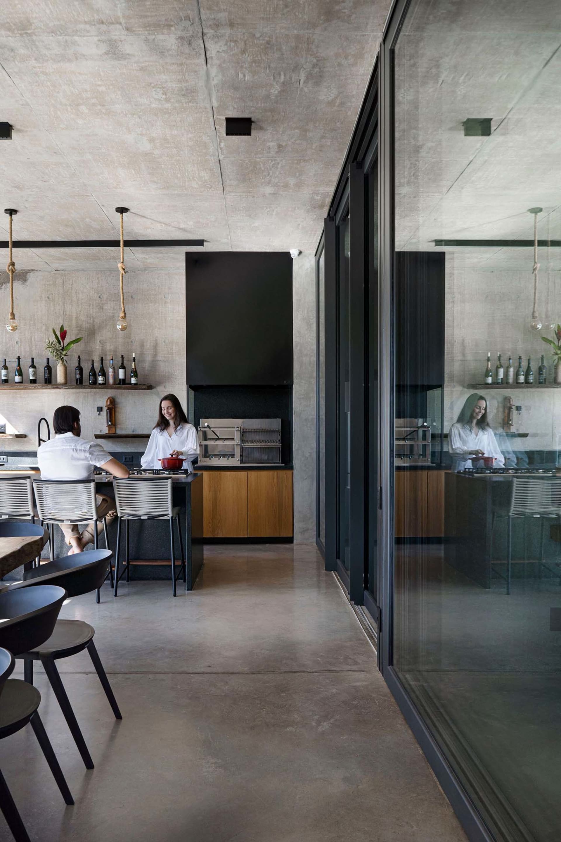 A modern industrial kitchen with a concrete countertop, hanging lights, and a woman preparing food