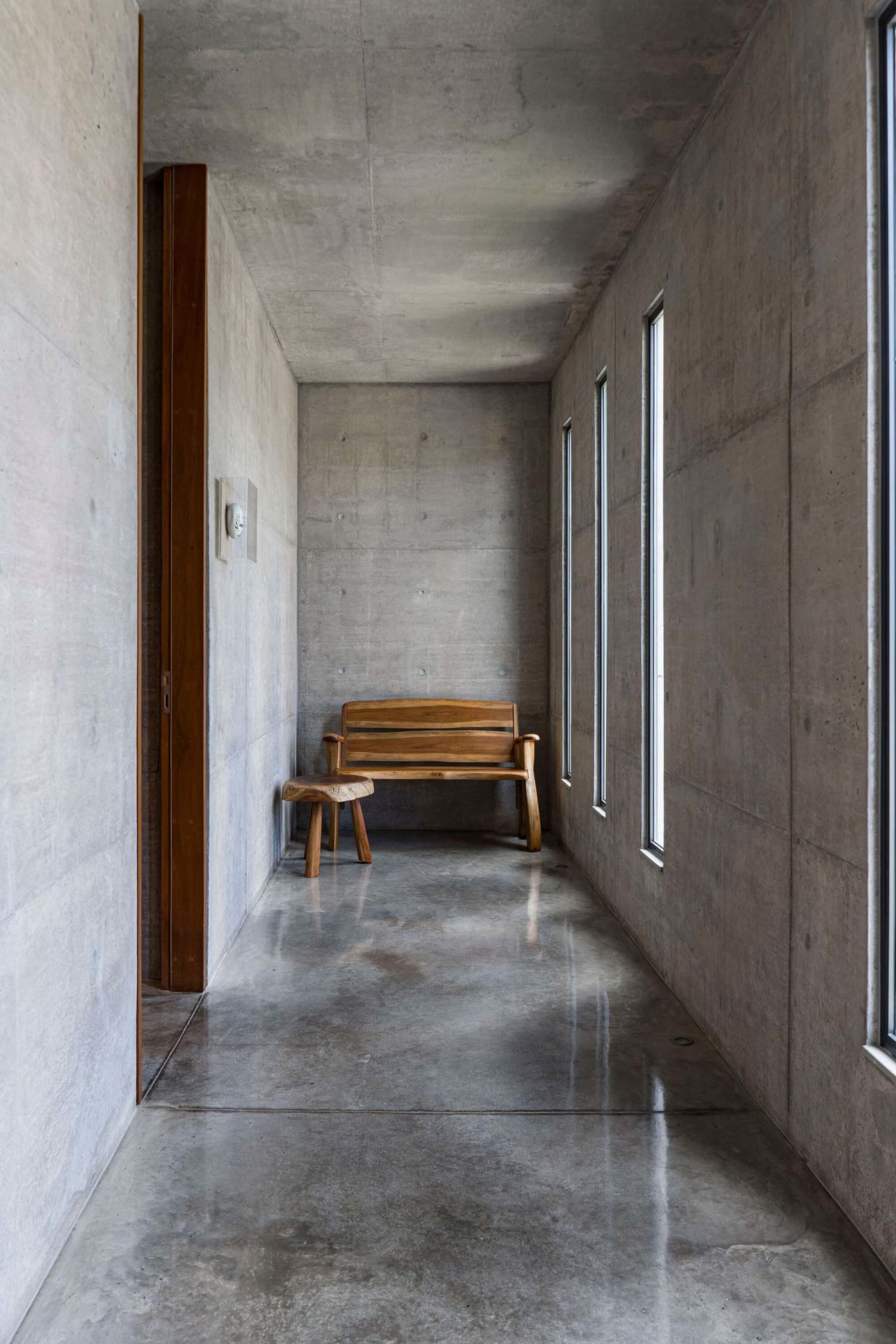 A minimalist, modern interior space featuring a concrete floor and walls, with a wooden bench in the center.