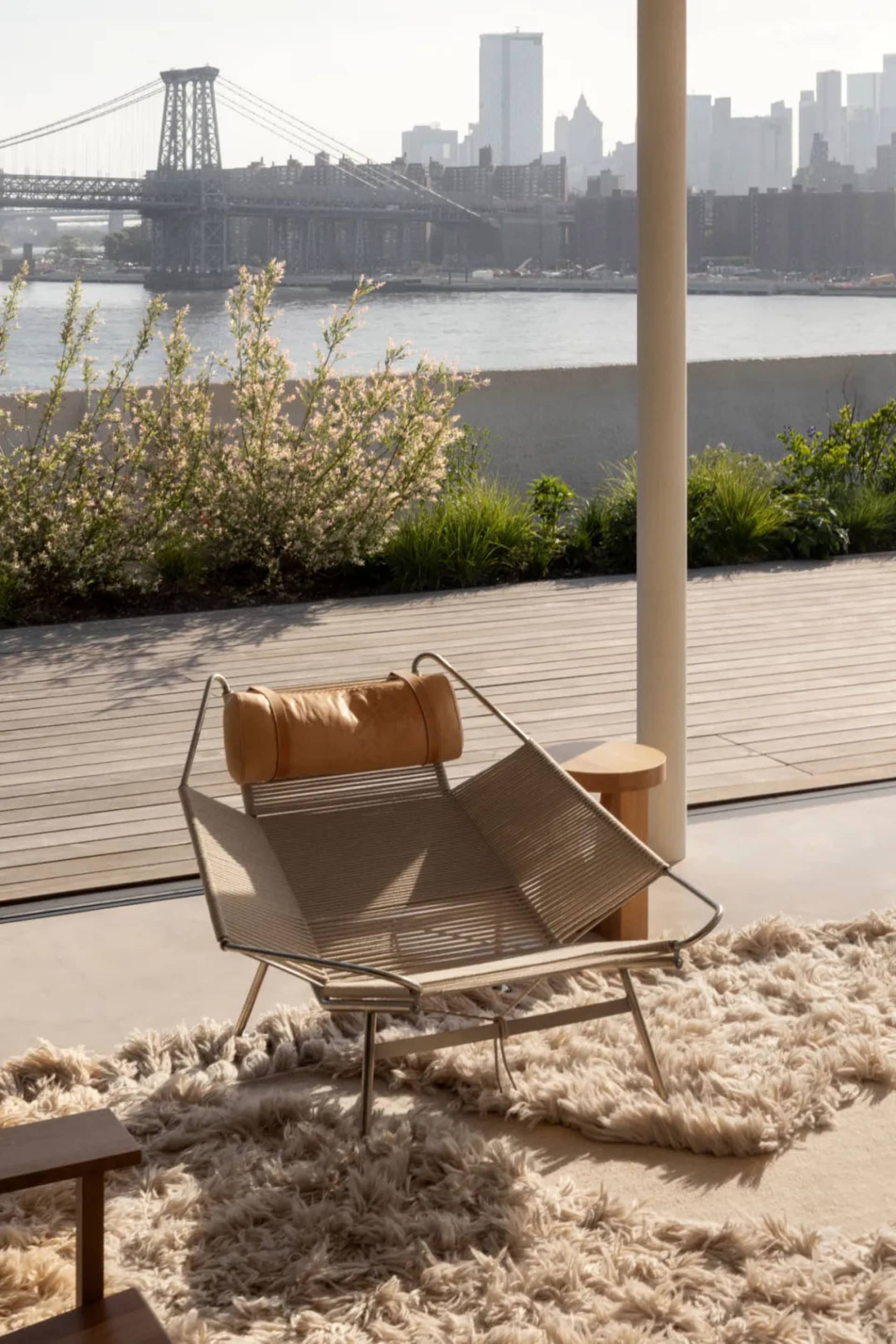 Modern rooftop lounge area featuring a leather-textile lounge chair with a wooden deck, plants, and a view of the city and br