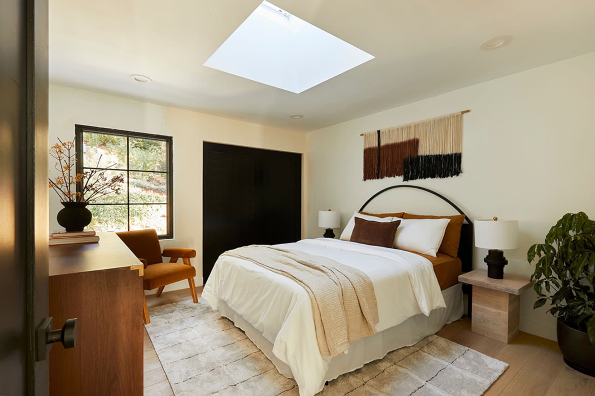 A minimalist bedroom with a white bed, brown cushions, and a skylight above a wooden floor.