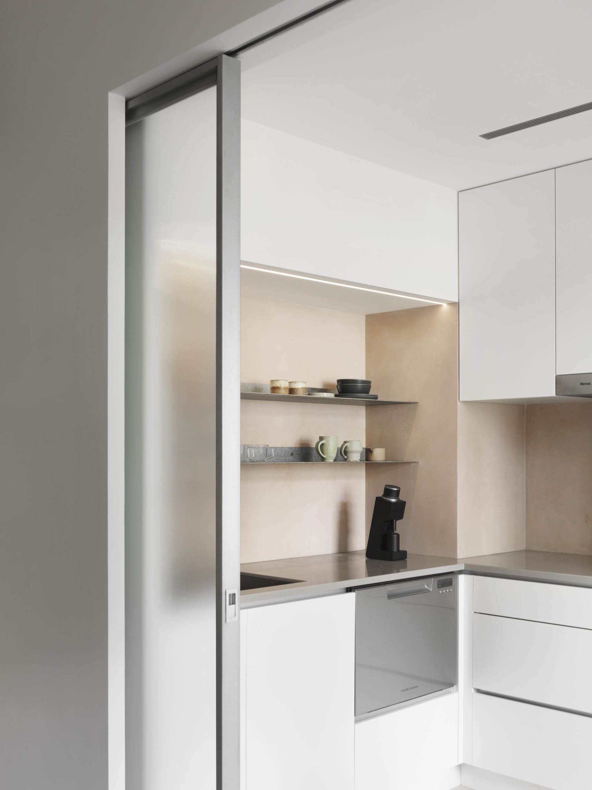 A modern, minimalist kitchen with white cabinets, open shelves, and sleek, clean lines.