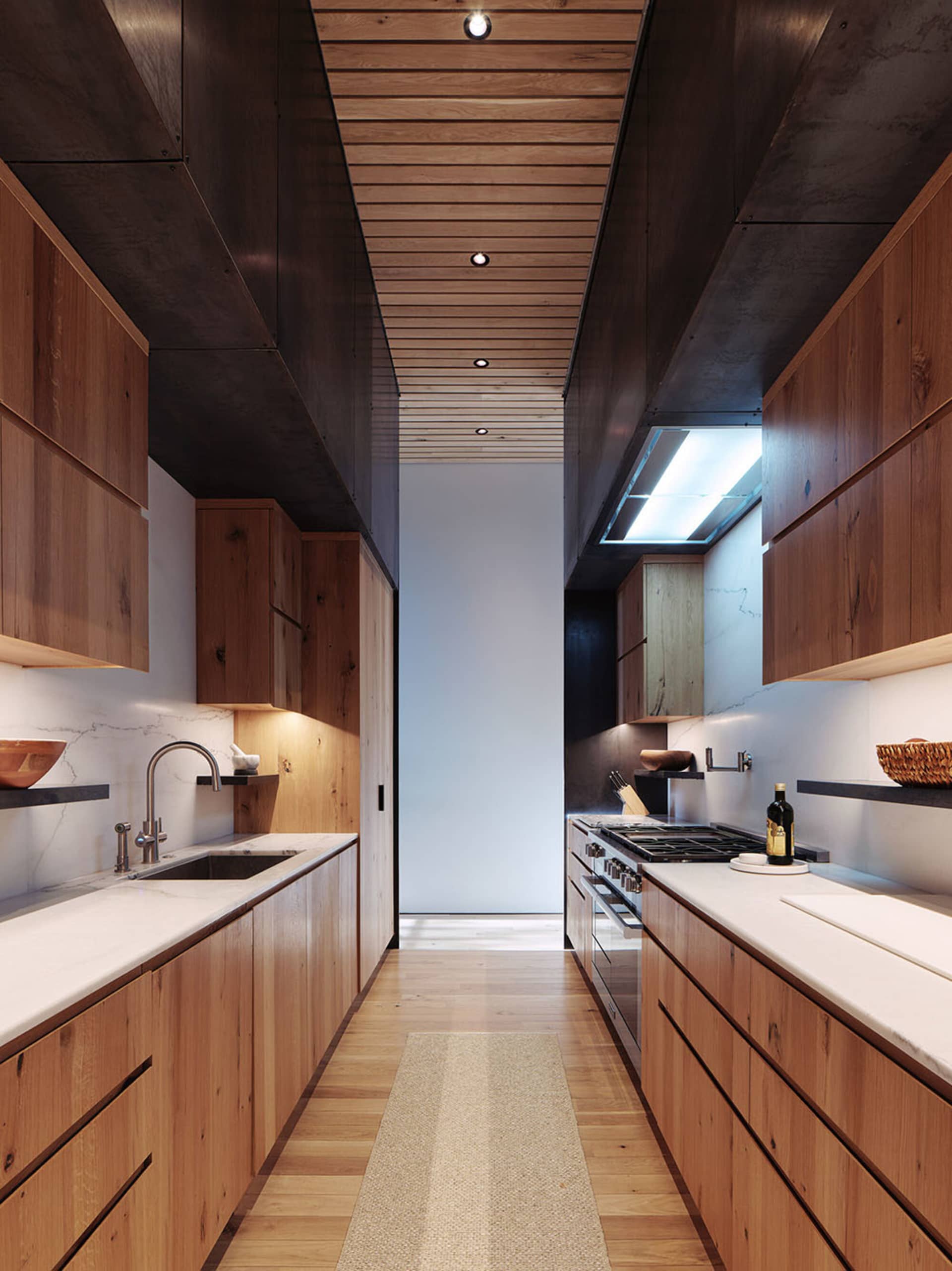 A modern kitchen featuring wooden cabinets and countertops, with a long hallway layout.