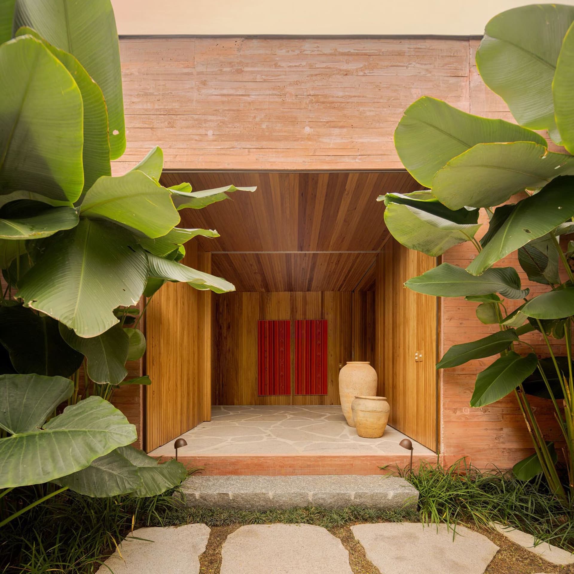 Modern minimalist entrance featuring wood and stone materials, with large plants flanking the doorway.