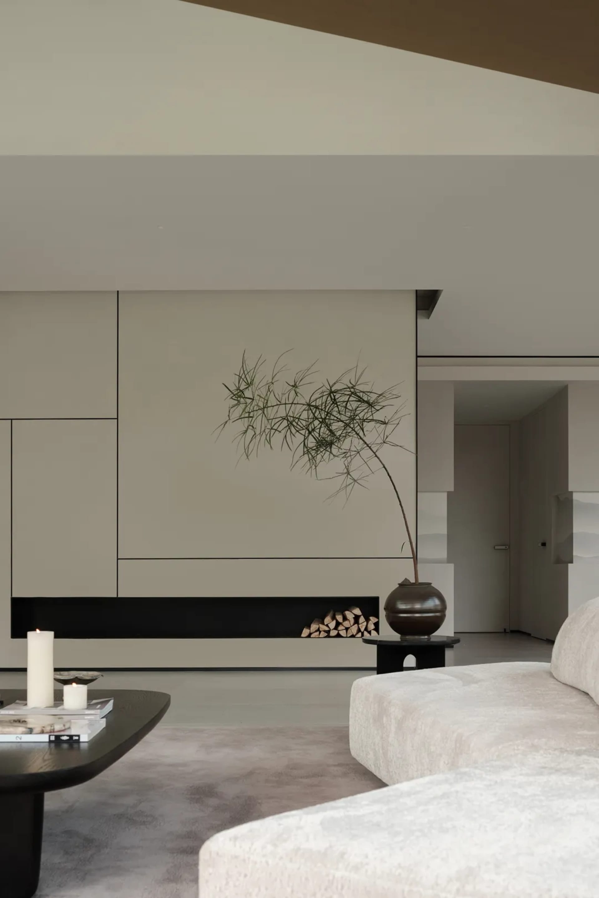 A minimalist living room features a sleek, modern fireplace, a white sofa, and a low coffee table with candles and books.