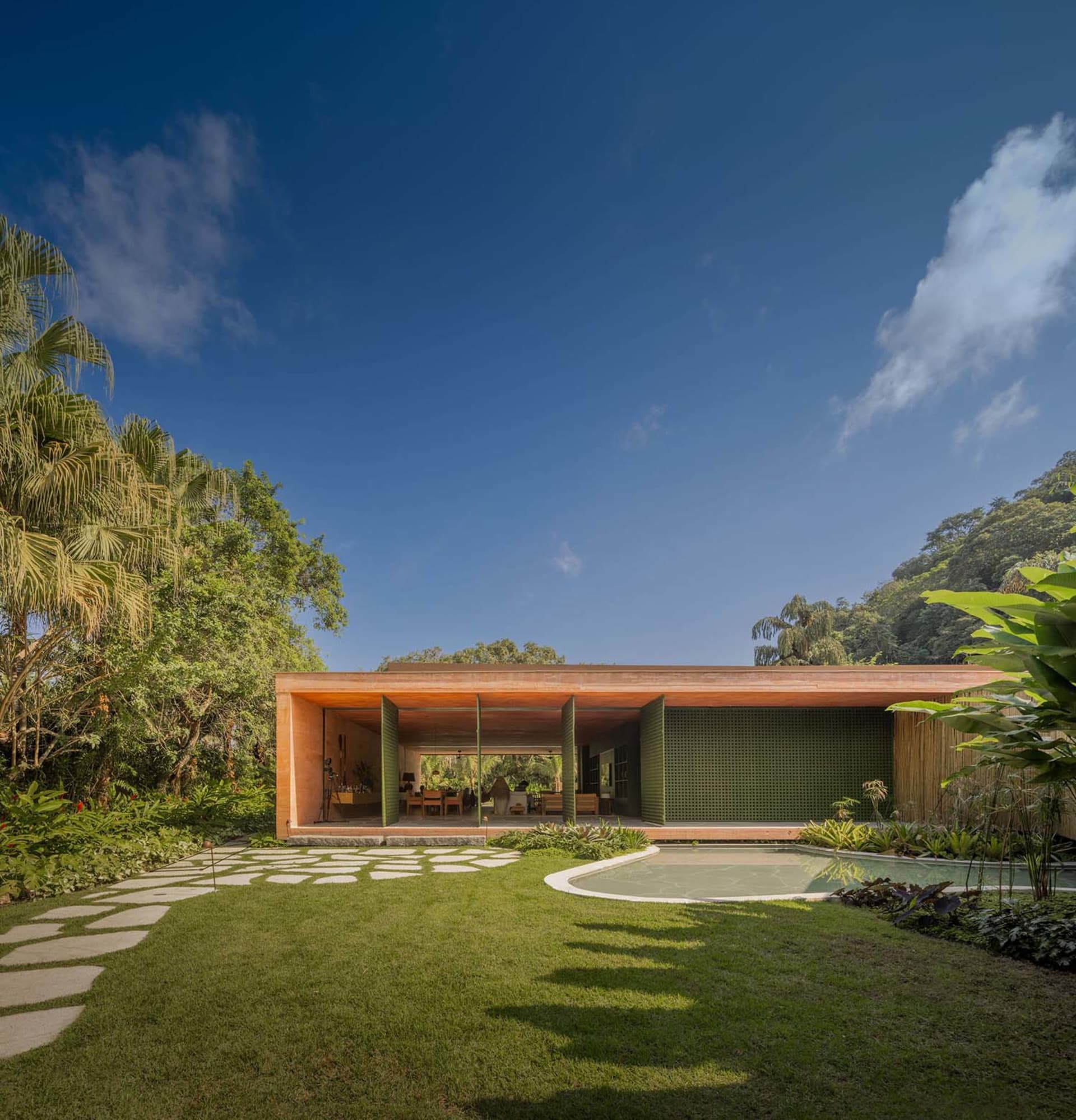 A modern architectural design featuring a concrete structure with wooden framing, surrounded by lush greenery and a swimming