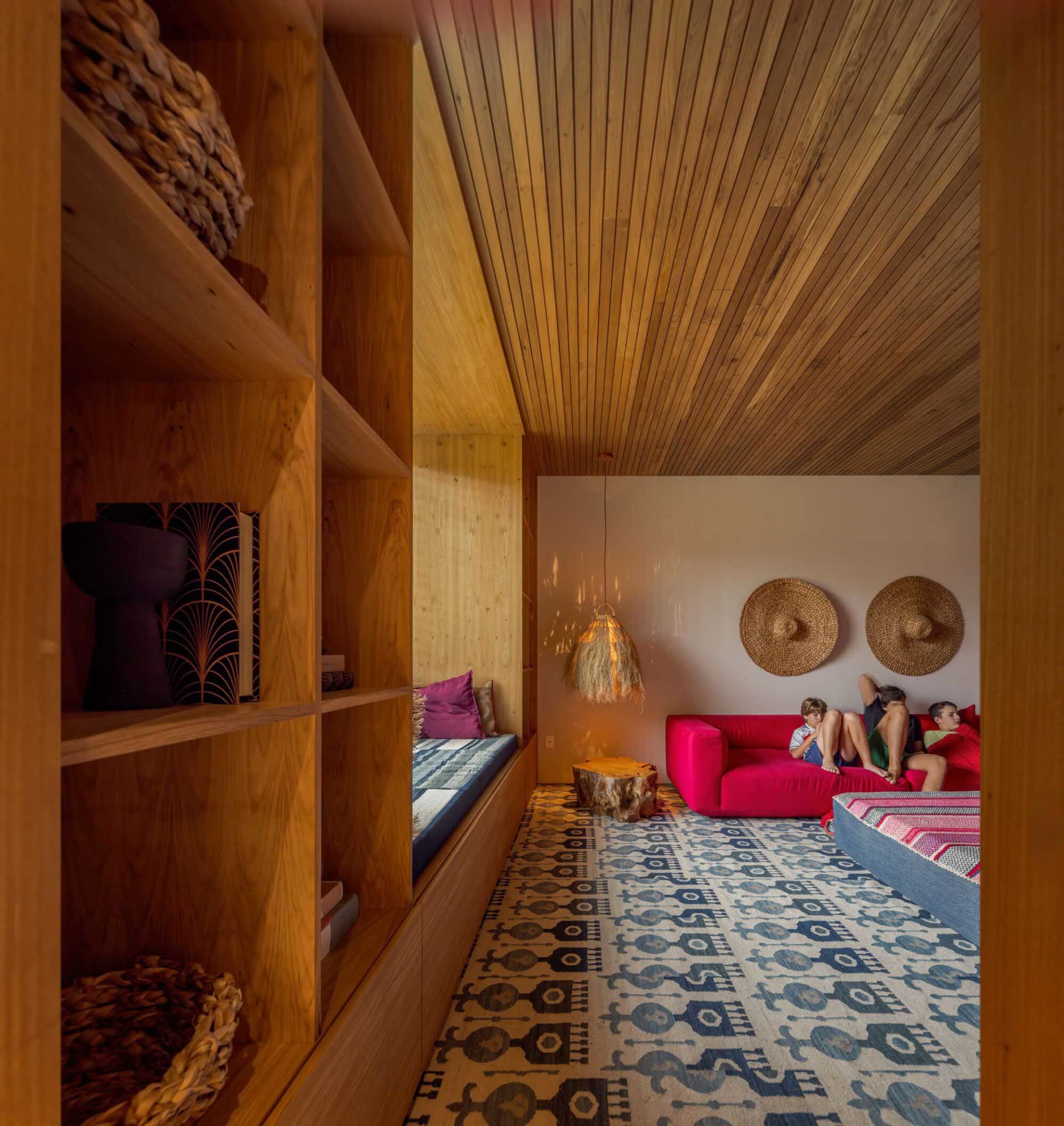 A cozy modern living room with wooden furniture and a vibrant pink sofa, featuring built-in shelves, a patterned rug, and wov