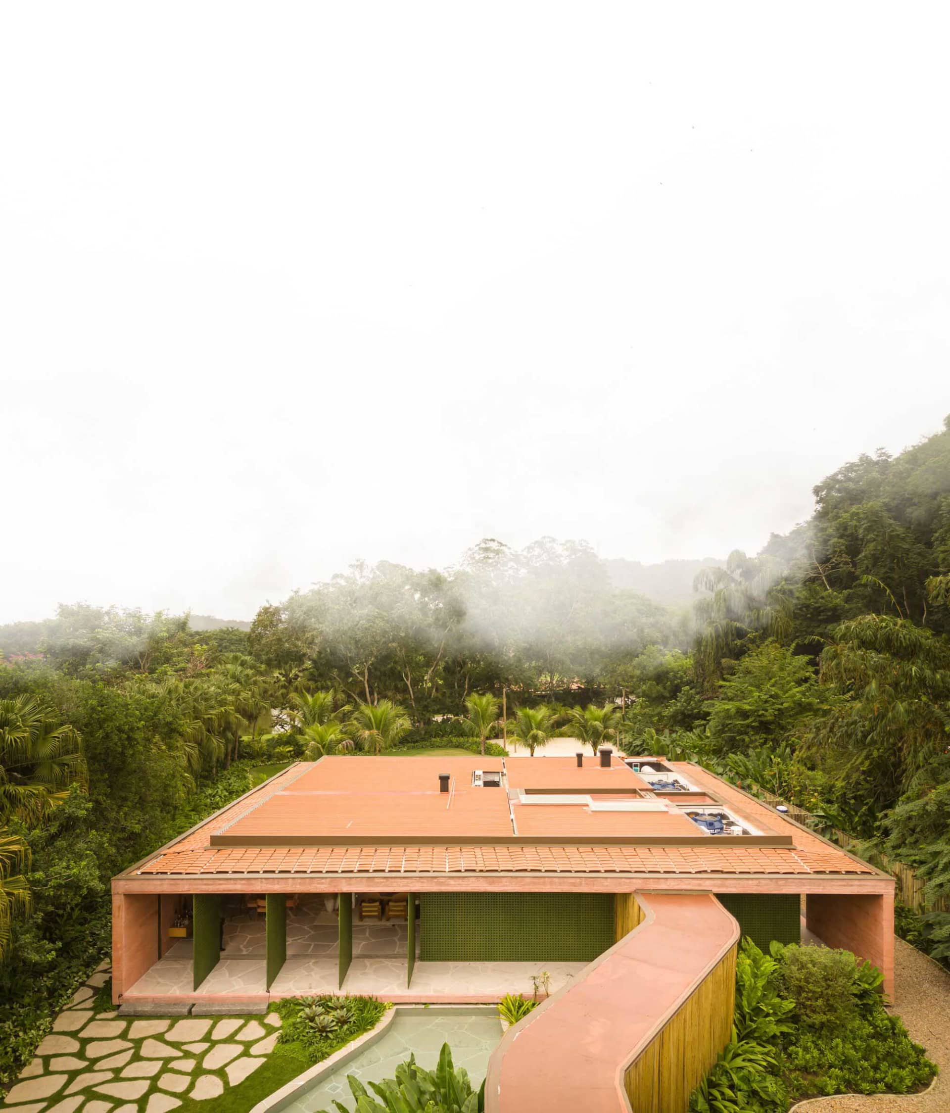 一座現代住宅建築,擁有陶土屋頂與混凝土牆面,周圍環繞著茂密的綠色植被。