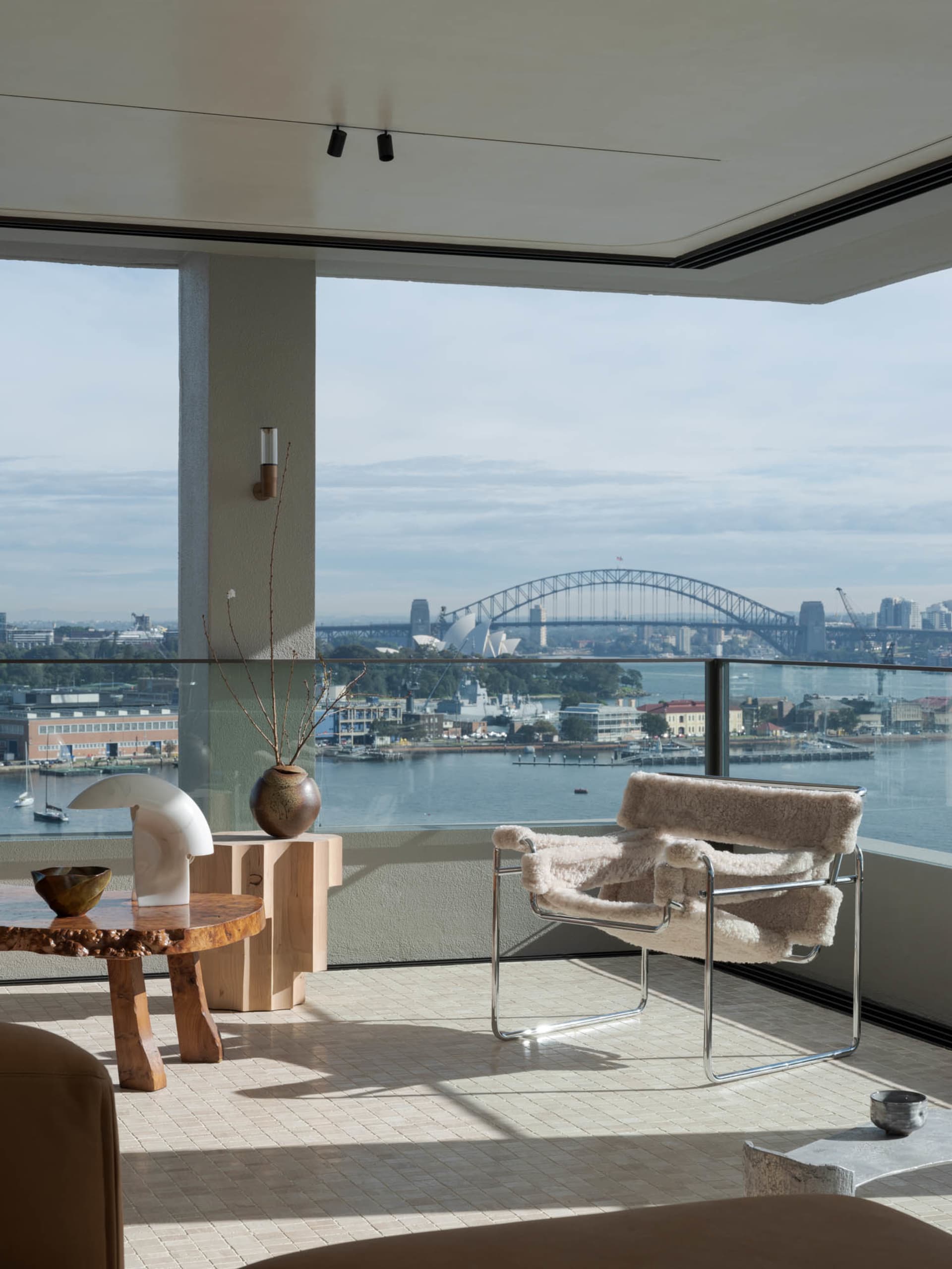 A modern minimalist living room with a view of a cityscape featuring the Sydney Harbour Bridge and the Sydney Opera House.