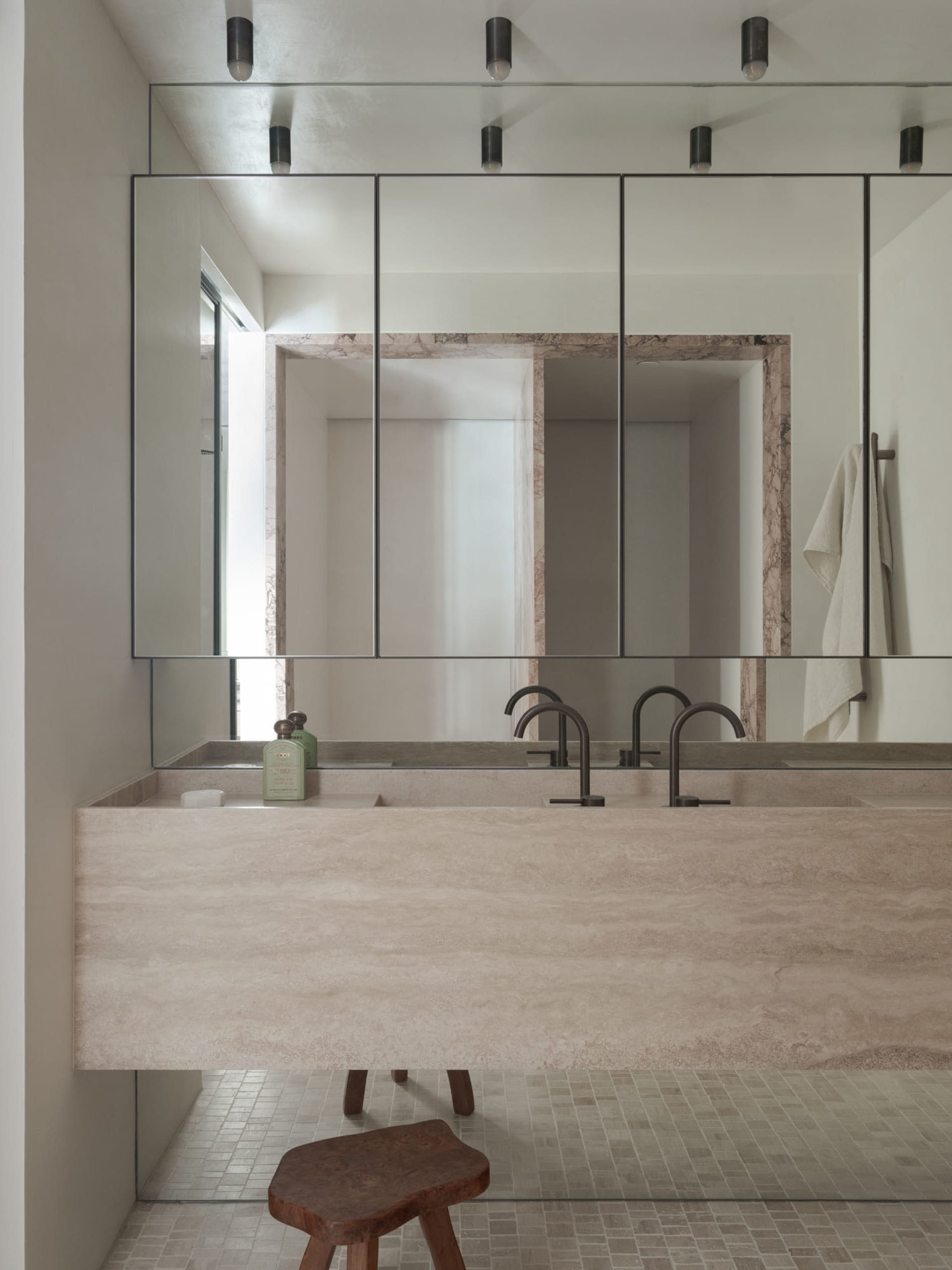Modern minimalist bathroom with a large rectangular sink counter made of marble, a large mirror above it, and a stool underne