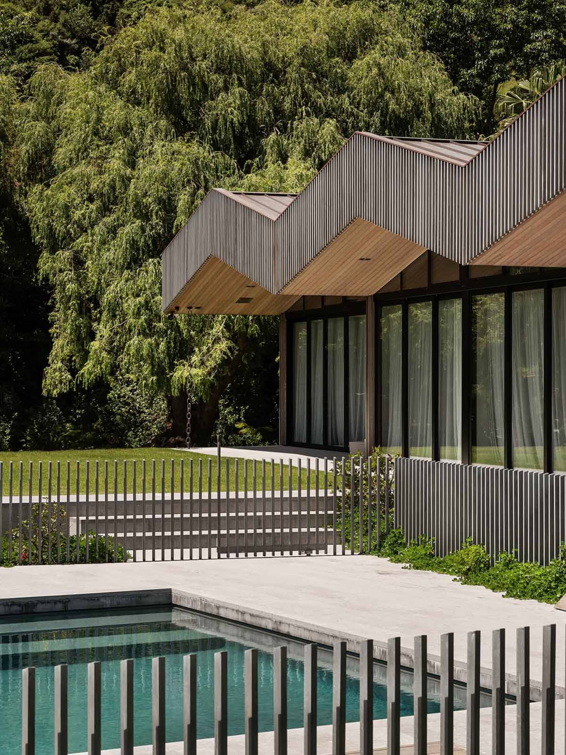 Modern minimalistic house featuring concrete exterior walls, a swimming pool with a metal fence, and a lush green courtyard w
