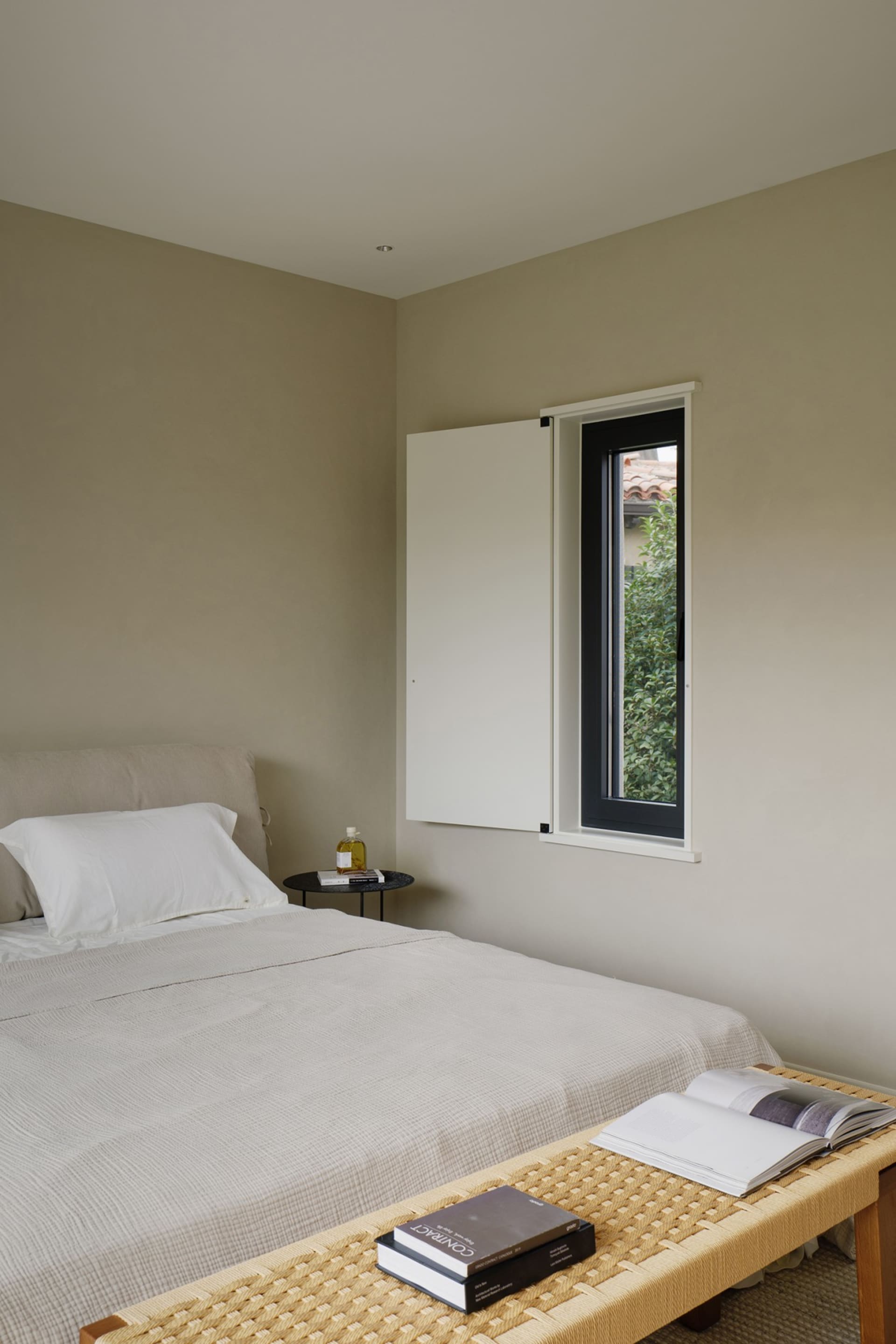 A minimalist bedroom with neutral-toned textiles and a window showing greenery outside.
