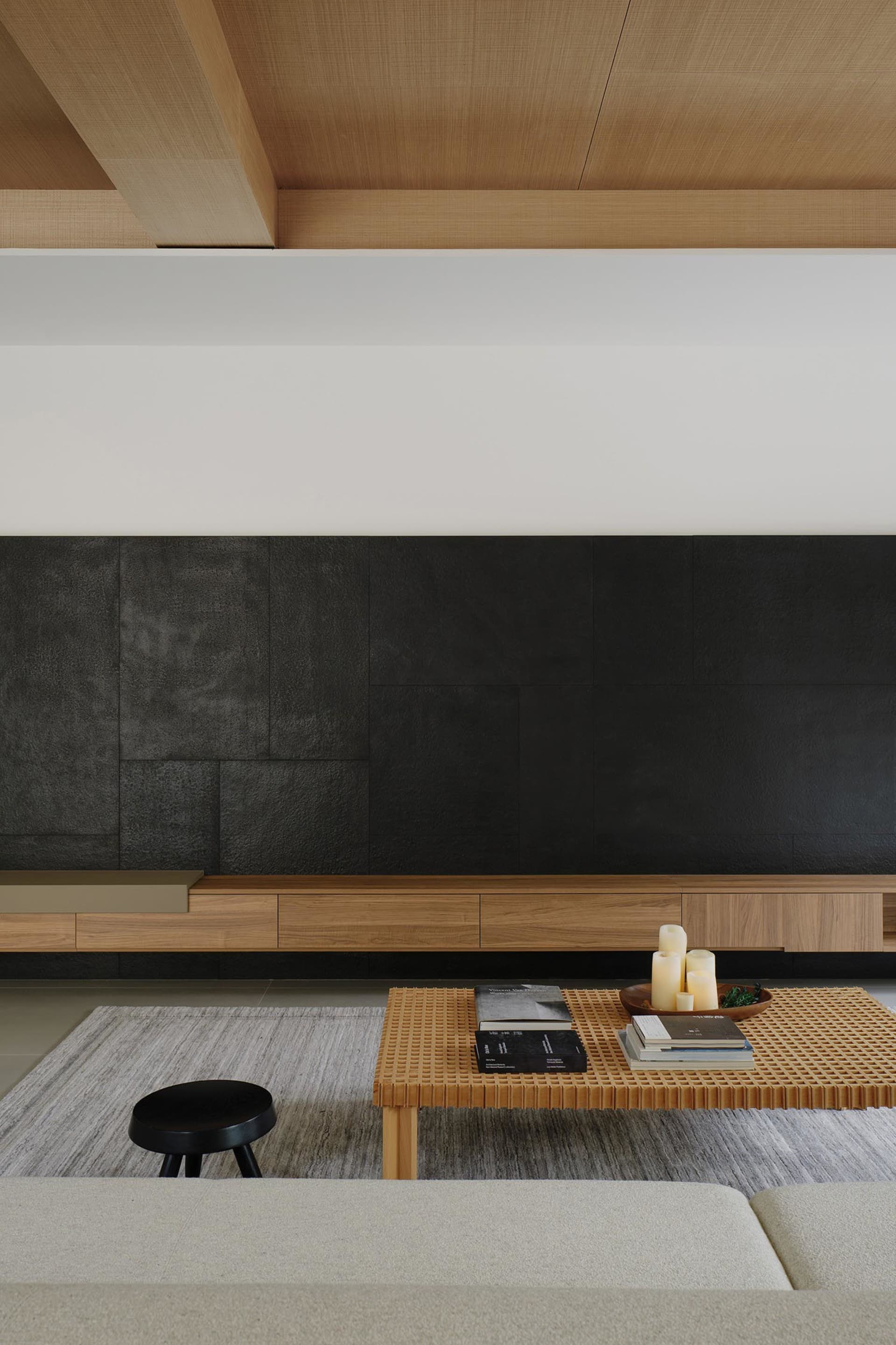 A minimalist living room with wooden furniture and a textured black wall.