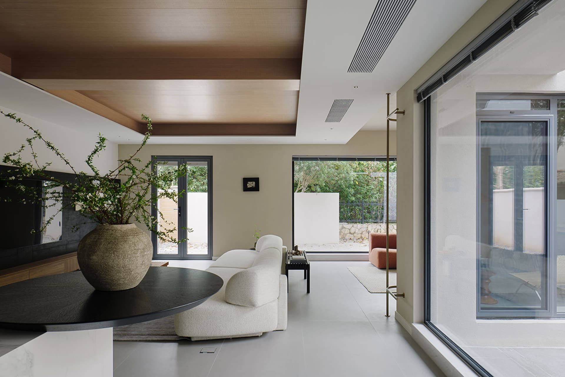 Modern minimalist living room with white upholstered furniture, marble flooring, and large windows overlooking greenery.