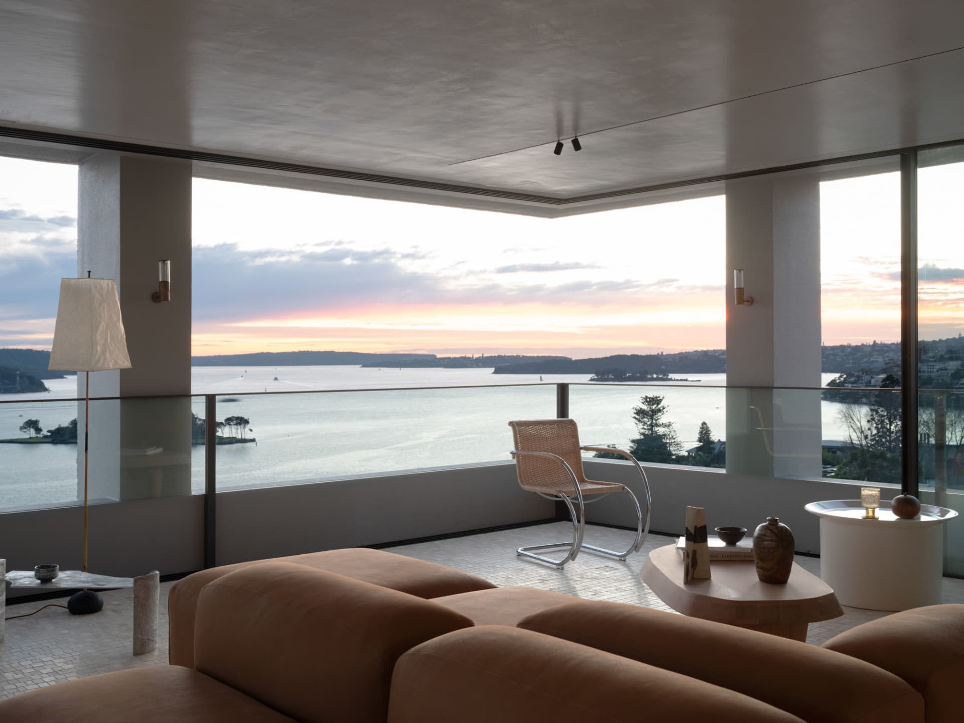 A minimalist living room featuring a modern leather sofa, a glass coffee table with ceramic ornaments, and a view of the sea