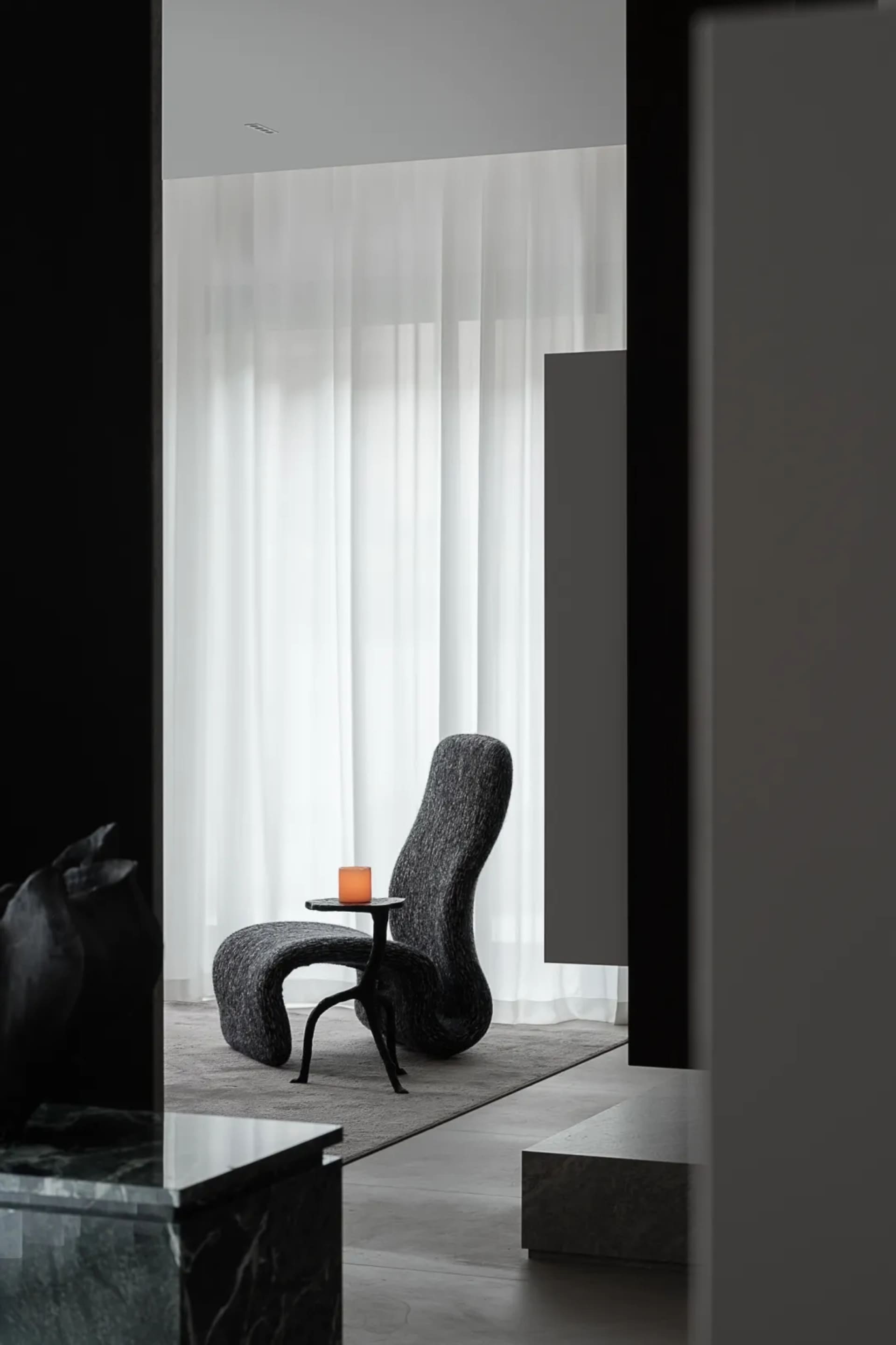 Modern living room with a black fabric chair and a lit candle on a small table.