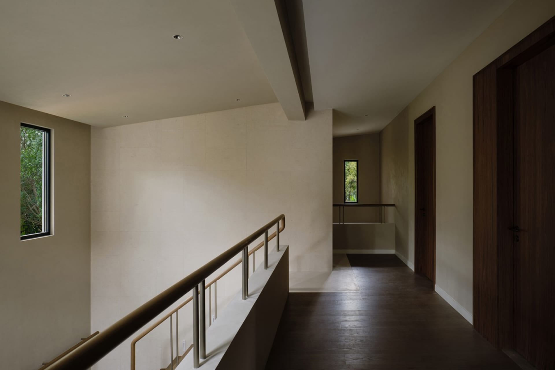 A minimalist hallway with wooden flooring and railings, featuring a small window overlooking greenery.