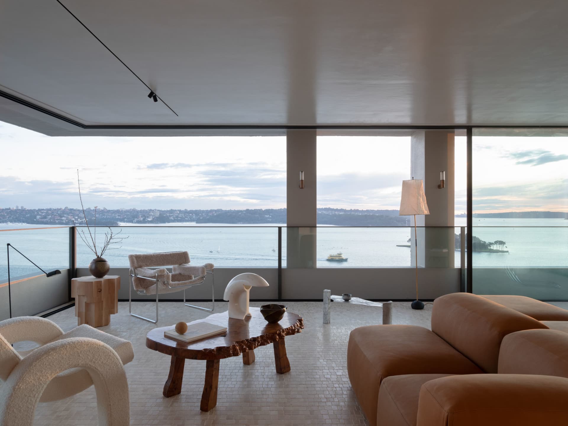 A modern residential living room featuring natural wood and concrete furniture with a view of the water.