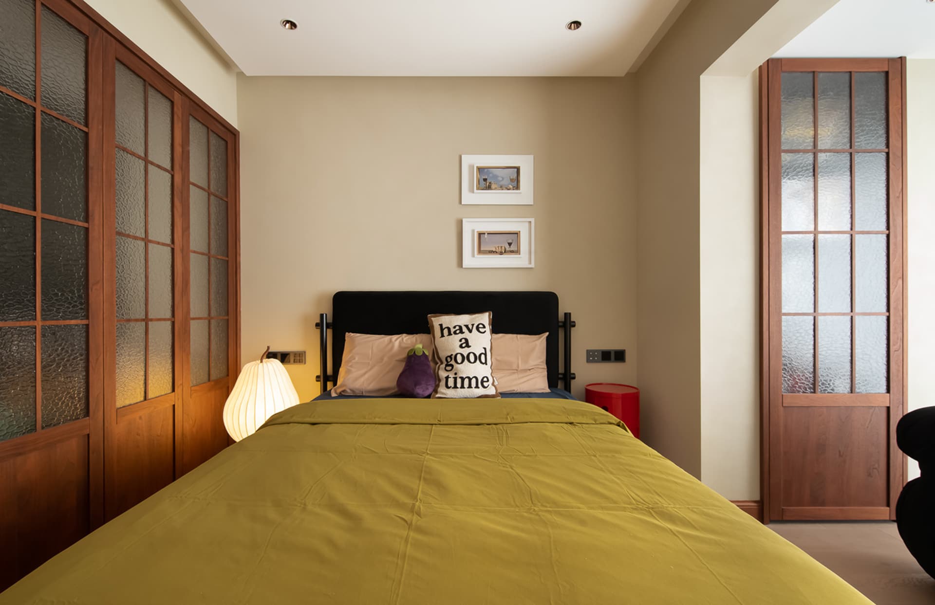 A minimalist bedroom with a yellow bed, black and white pillows, and a black headboard.