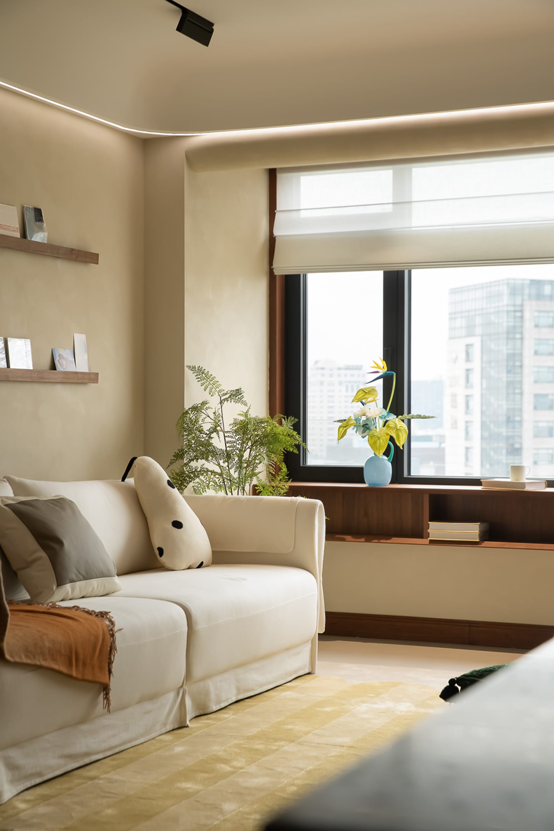 A modern minimalist living room with a white sofa, green plants, and a large window.