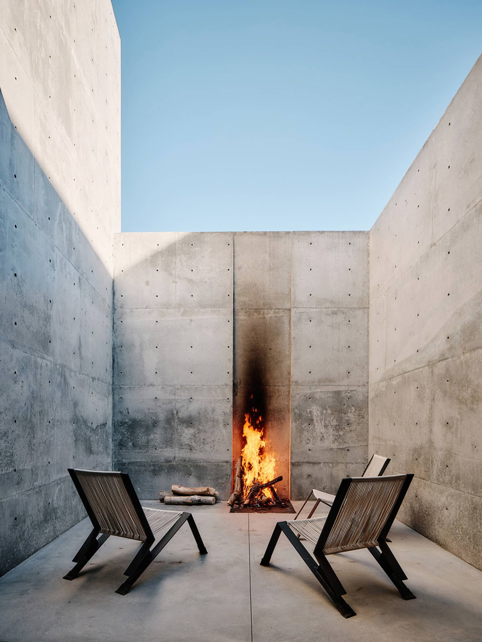 A modern concrete outdoor living space featuring a fire pit with flames