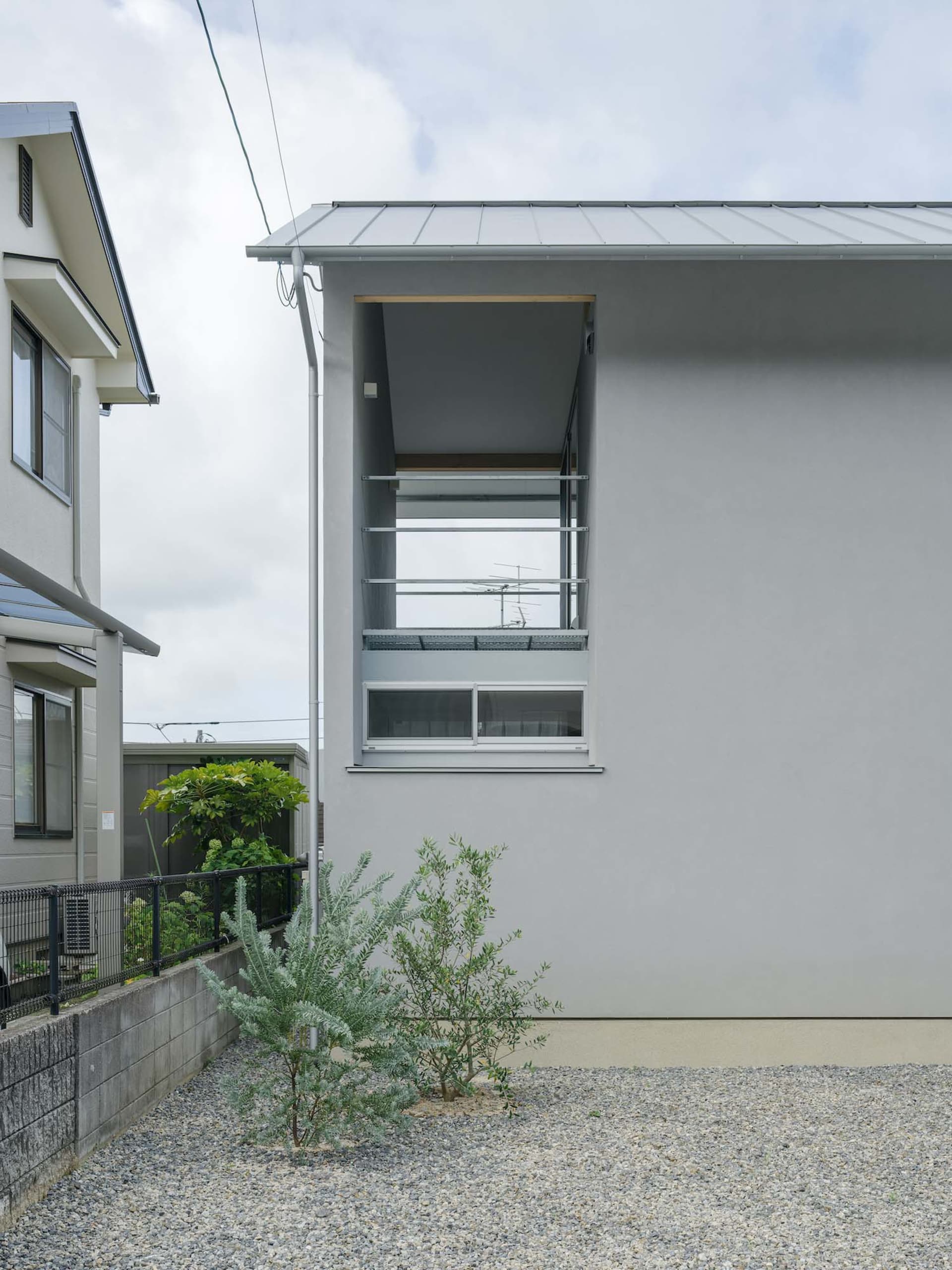 Modern residential house with concrete cladding exterior, small garden area with gravel and greenery, and minimalist architec