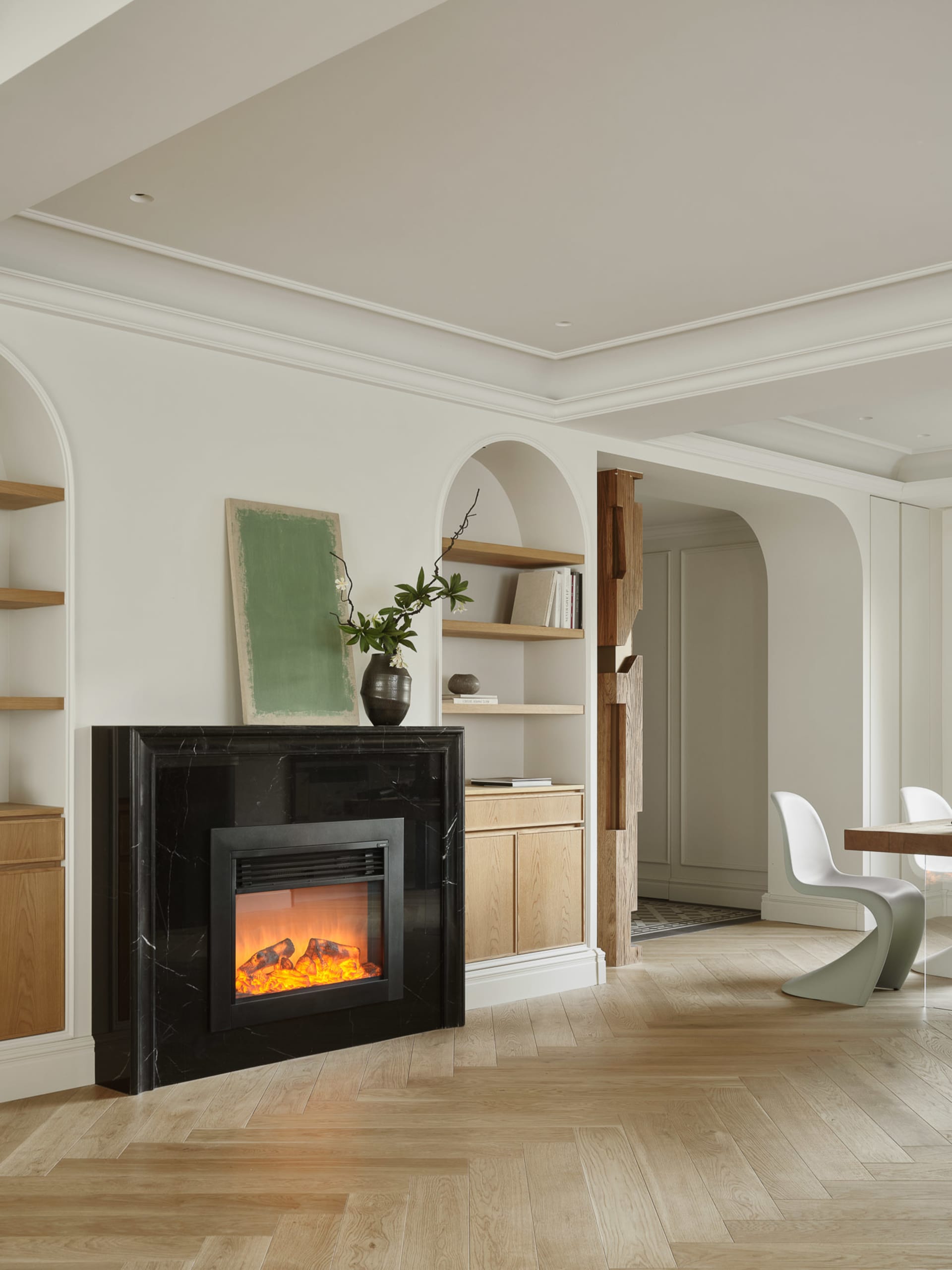 A modern minimalist living room featuring a black marble fireplace with a fire burning, surrounded by white walls and wooden