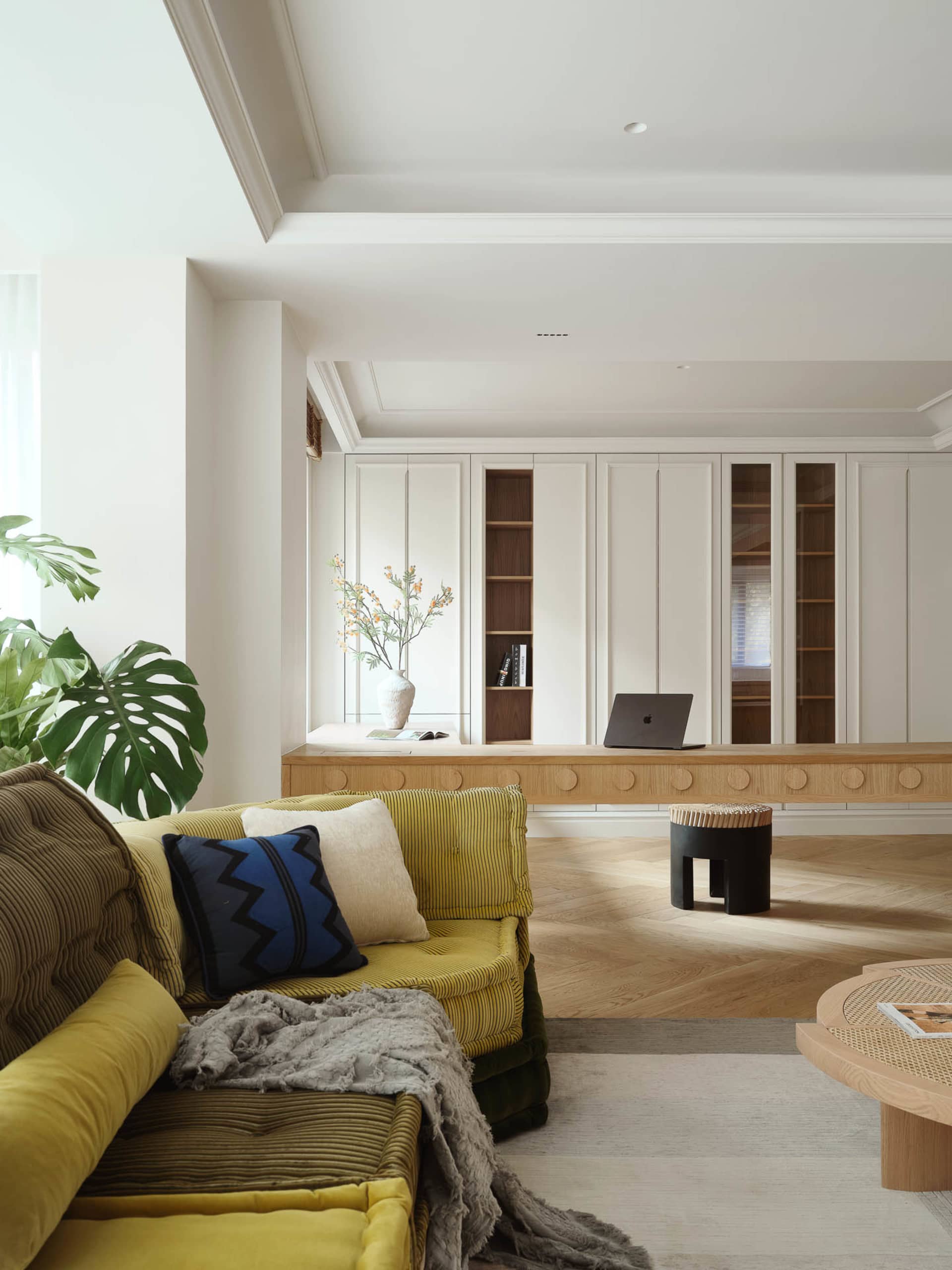 A modern living room featuring wooden furniture, a yellow couch, and a bookshelf with books.