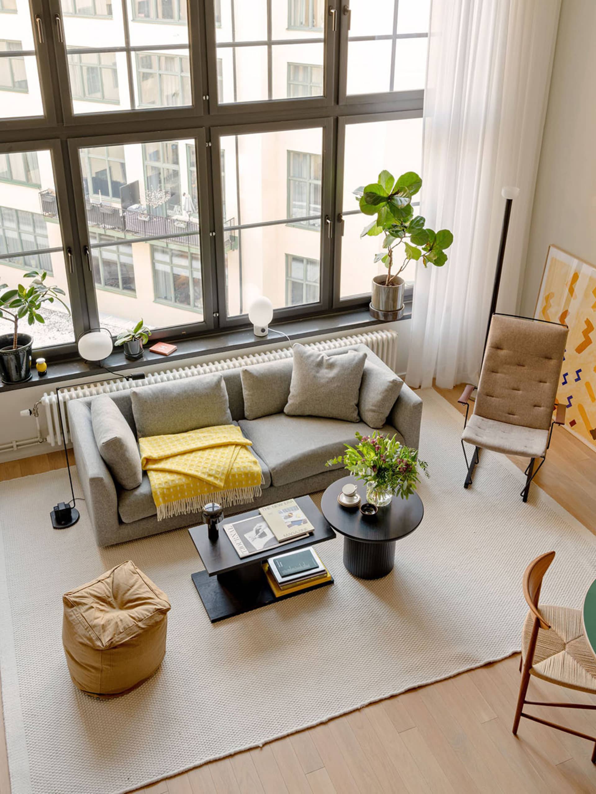 A modern, industrial-style living room featuring a grey sofa, a wooden coffee table, and potted plants.