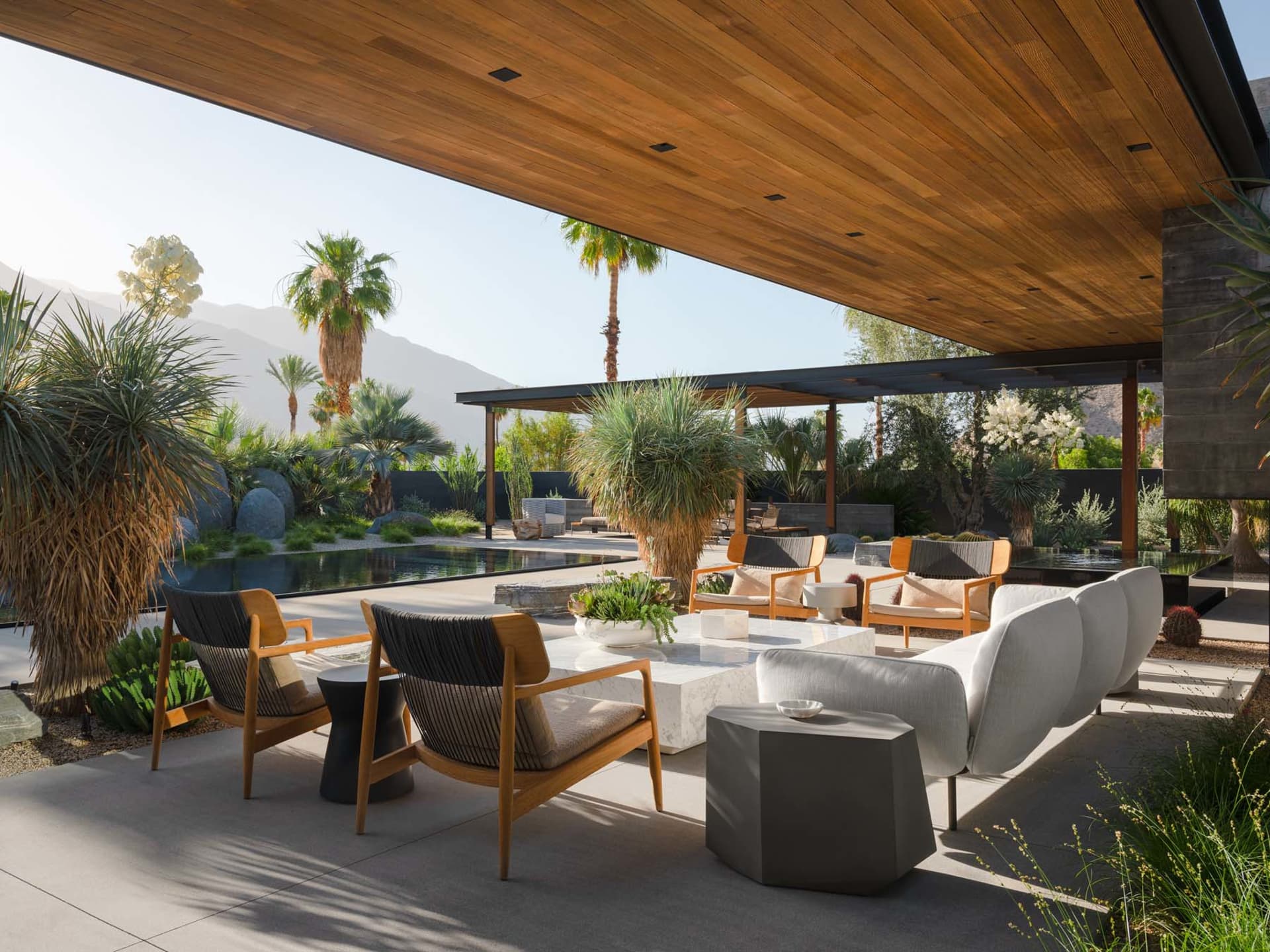Modern outdoor living space featuring wooden furniture, concrete floor, and glass walls.
