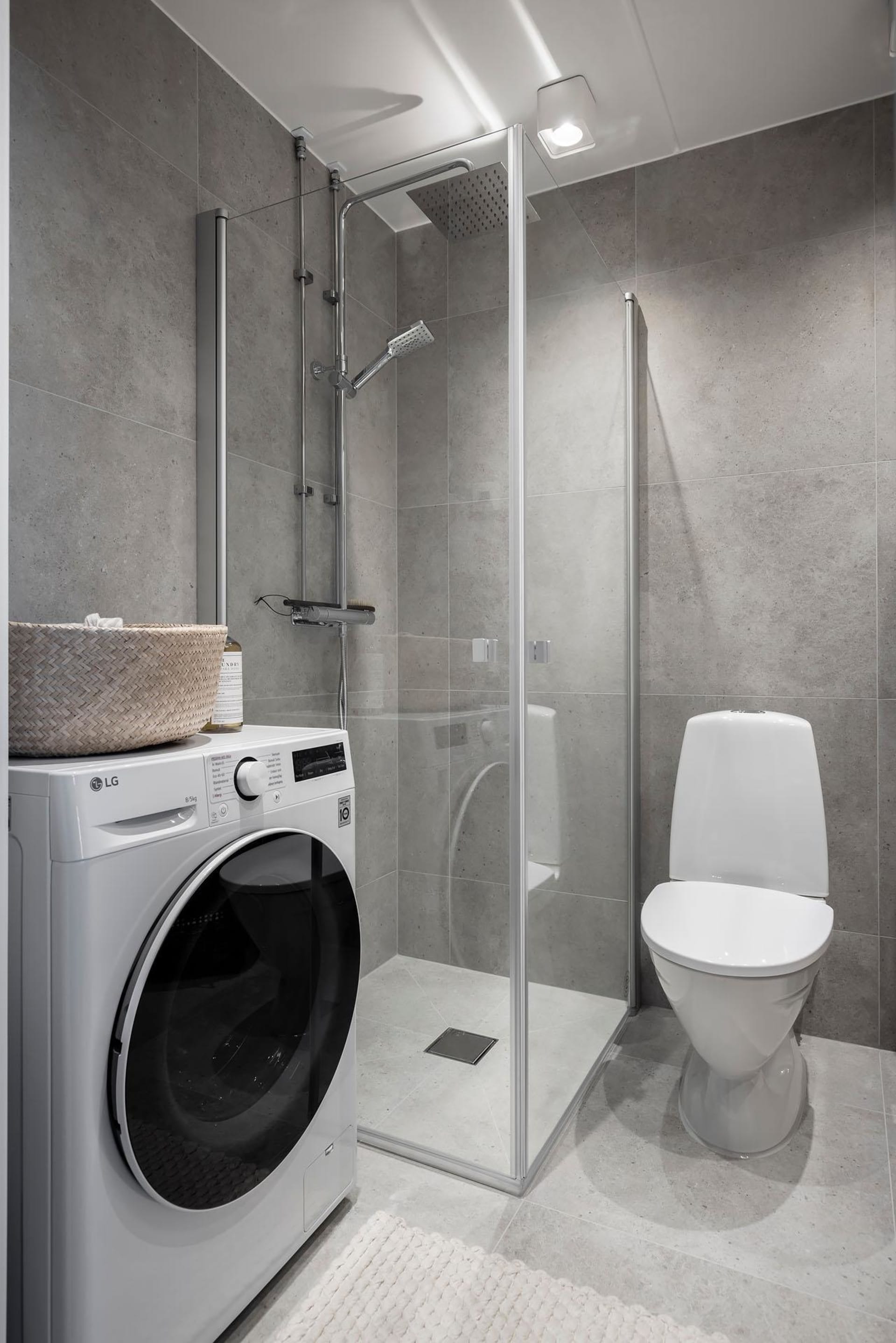 Modern bathroom with concrete walls, glass shower enclosure, washing machine, and toilet.