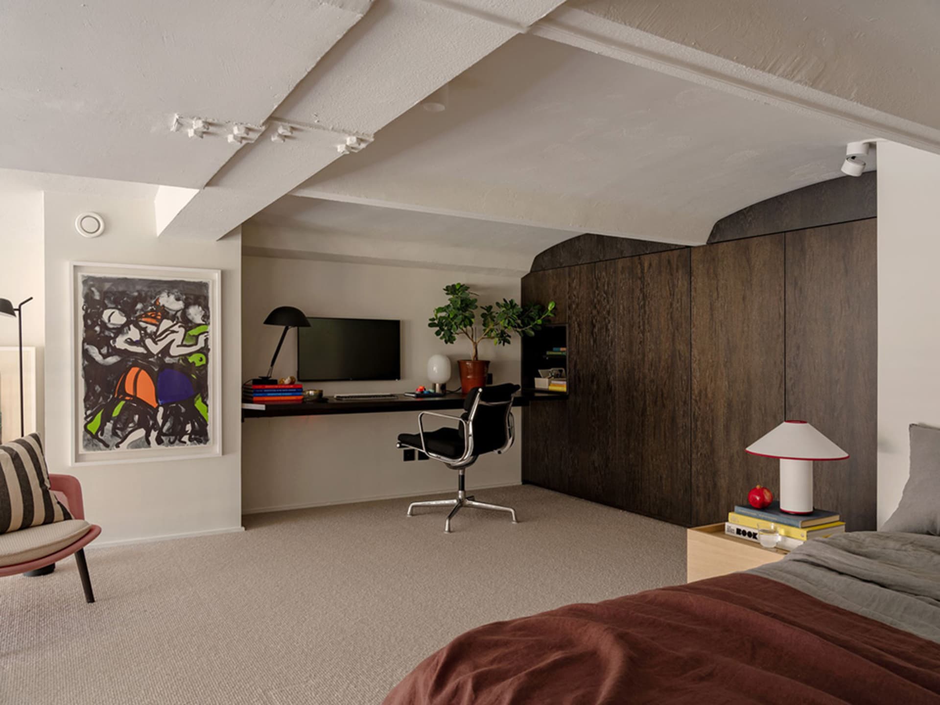 A stylish modern bedroom featuring a sofa, wood cabinets, and a sleek desk area.