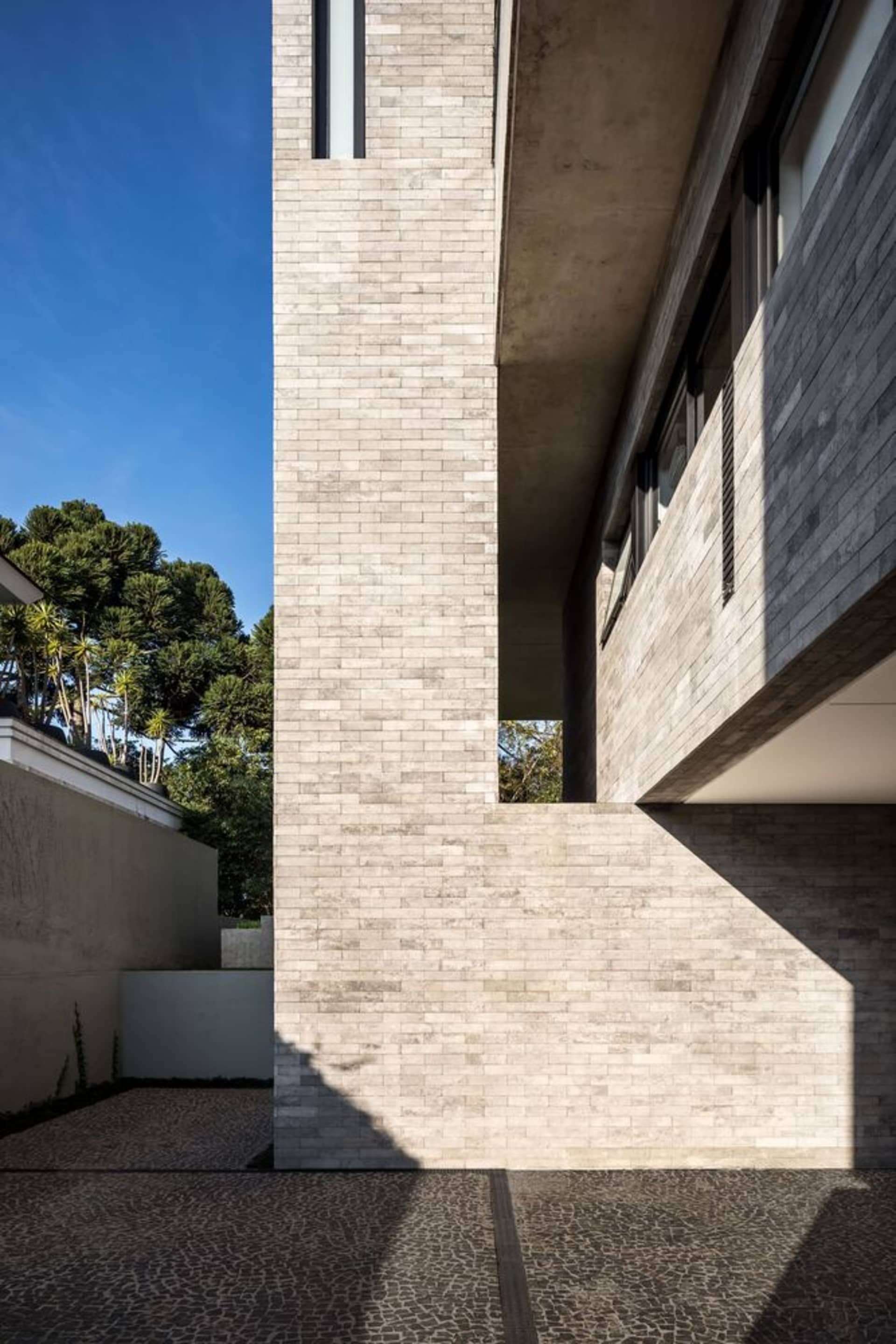 Concrete exterior of a modern house with tall brick wall and glass windows.
