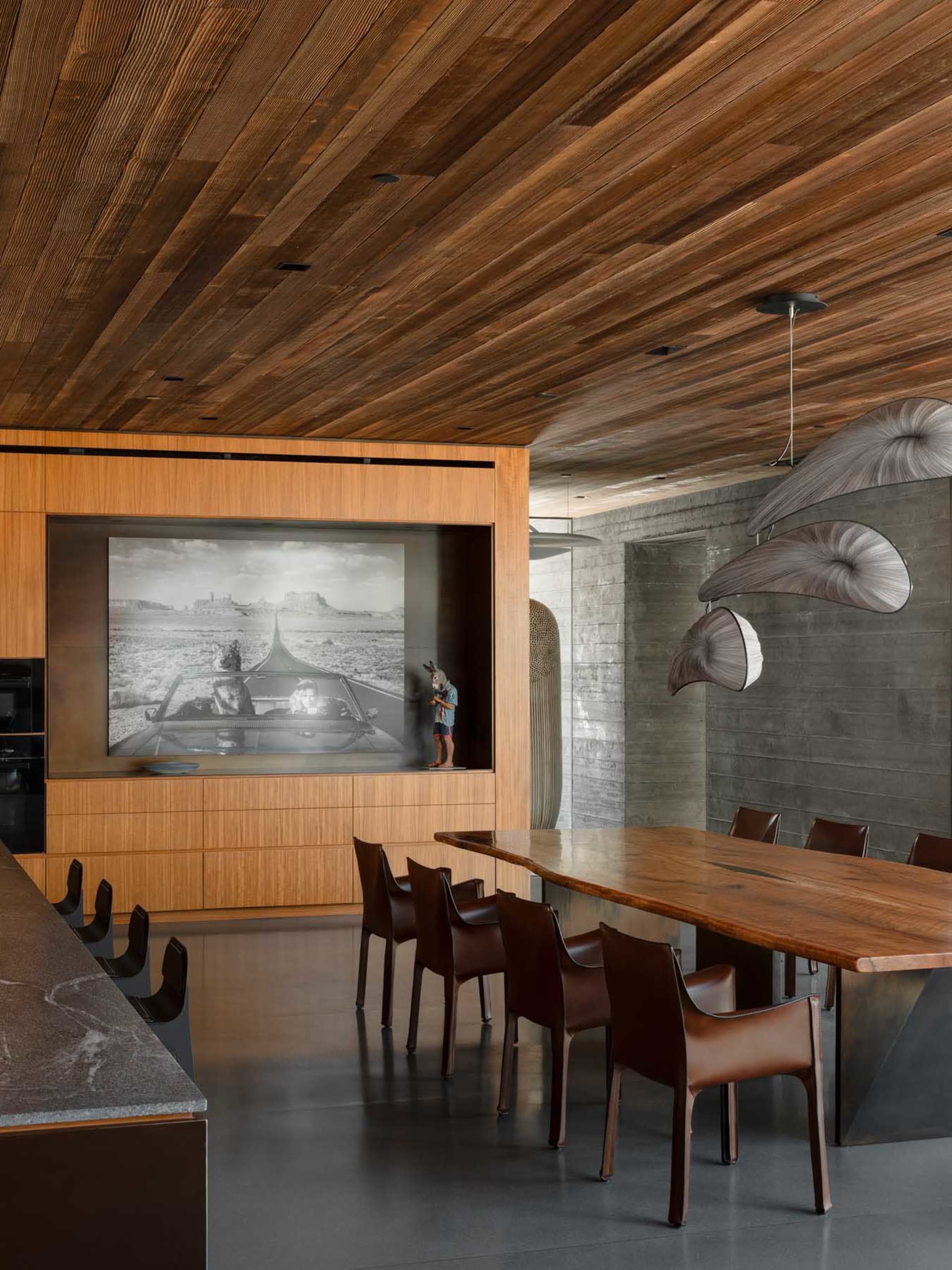 A modern dining room featuring a live-edge wood table and chairs, with a wooden ceiling and concrete elements.