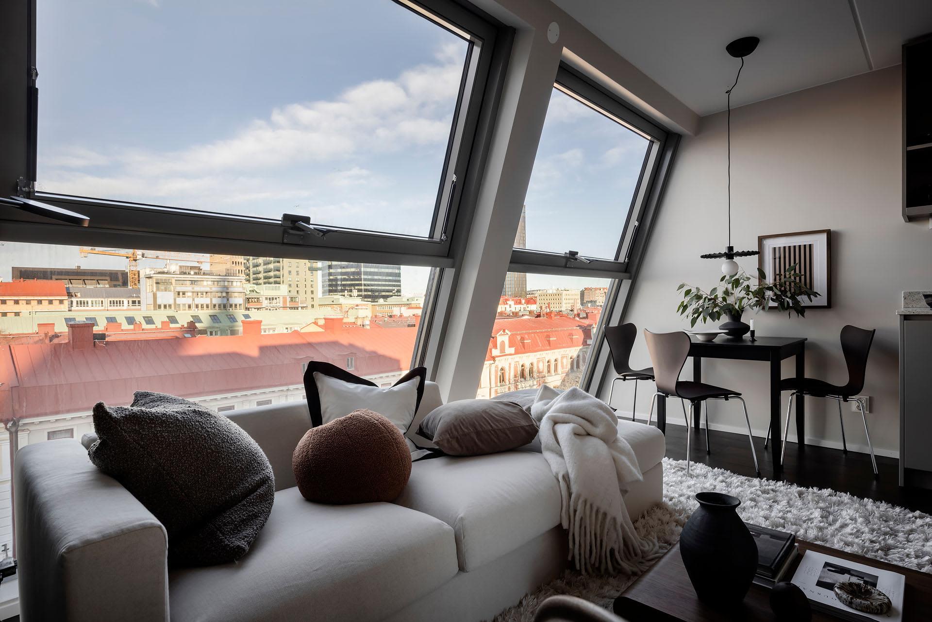 Modern living room featuring a white sofa, urban skyline, and large windows.