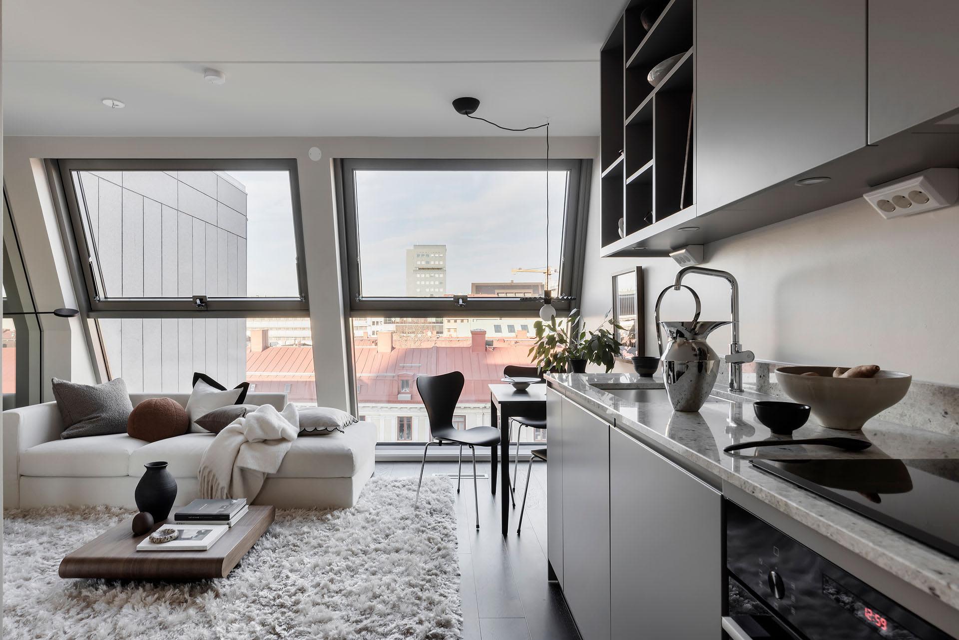 A modern living room with concrete, glass, and metal elements, featuring a white sofa, black chairs, and a minimalist design.