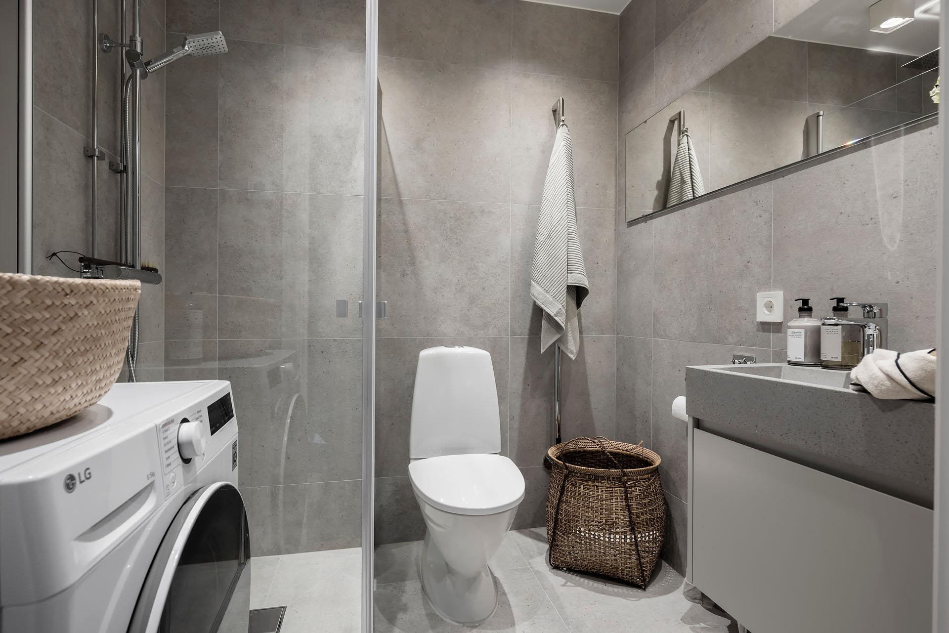 Photograph of a modern minimalist bathroom with concrete tiles on the walls and floor, featuring a white toilet, glass shower