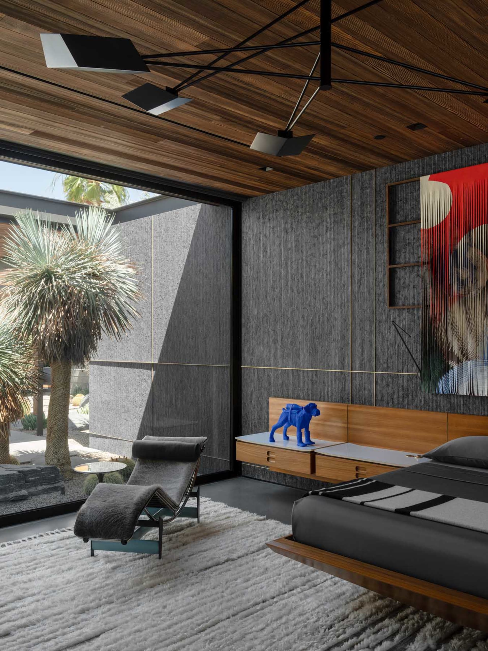 Modern minimalist bedroom featuring wood and glass elements with a blue dog statue on the bedside table and a plush rug on th