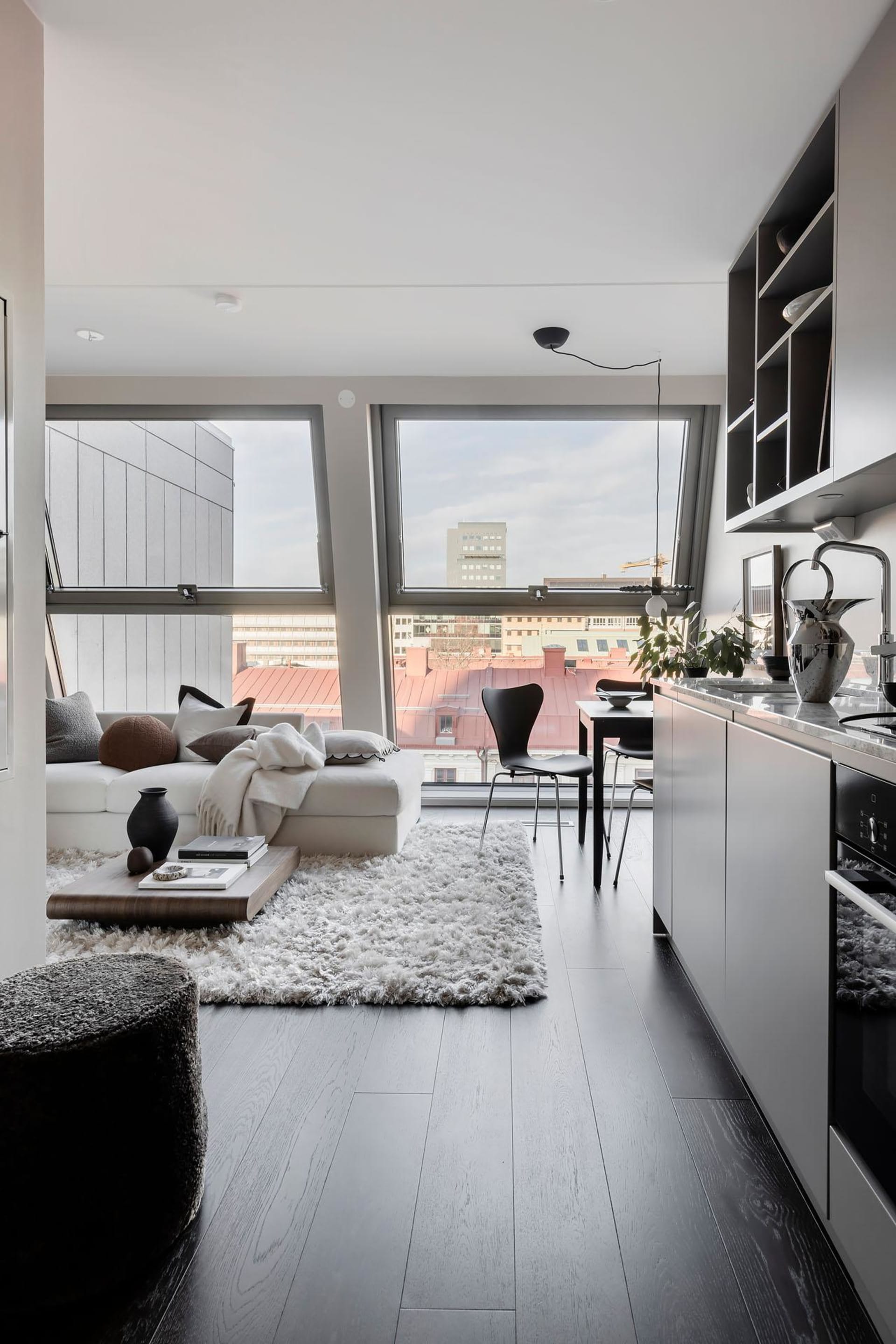A modern minimalist living room with a white couch, black chairs, and a wooden floor.