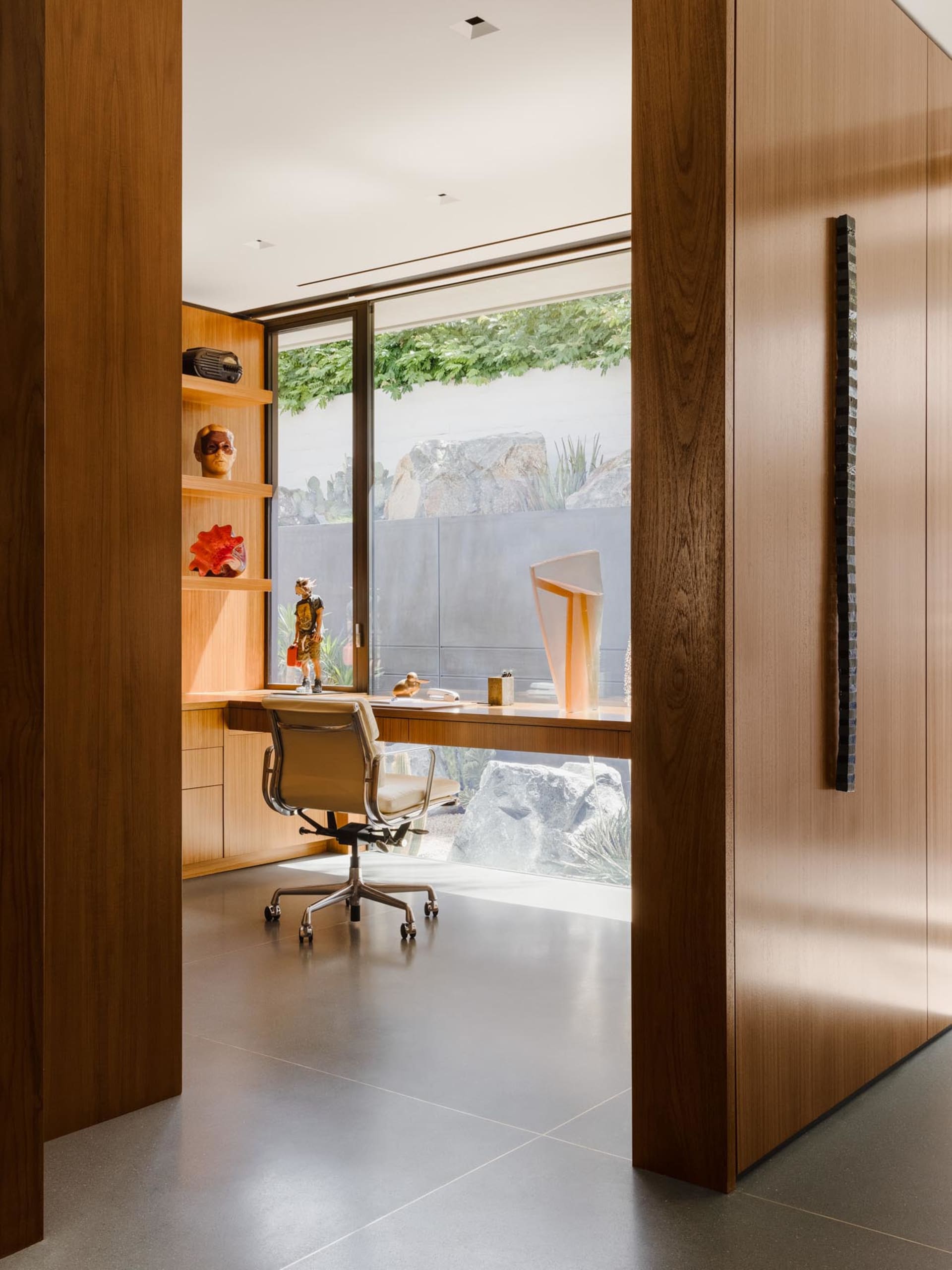 A modern office with a wooden workstation, featuring a comfortable chair and a window overlooking a garden.