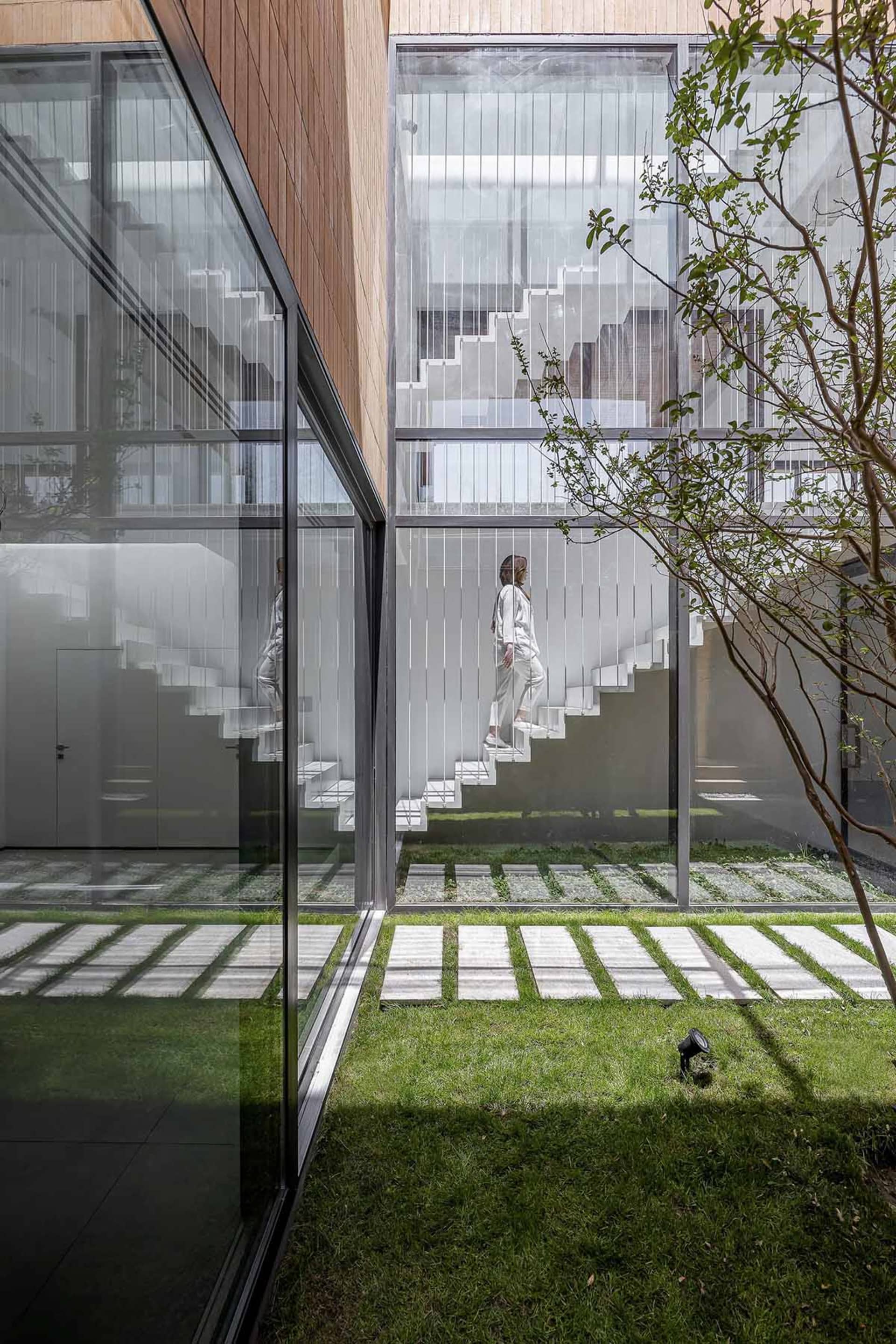 A modern residential building with glass and steel materials, featuring a clear glass courtyard and a person climbing stairs.