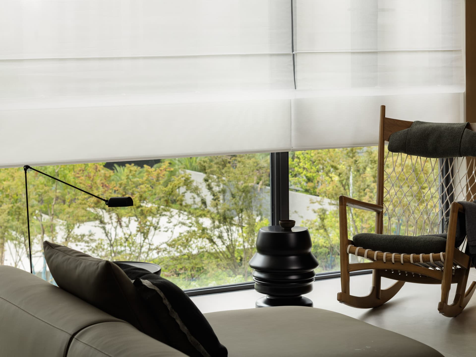 A modern living room featuring a white sofa with black accents, a rocking chair with green cushions, and a black floor lamp. 